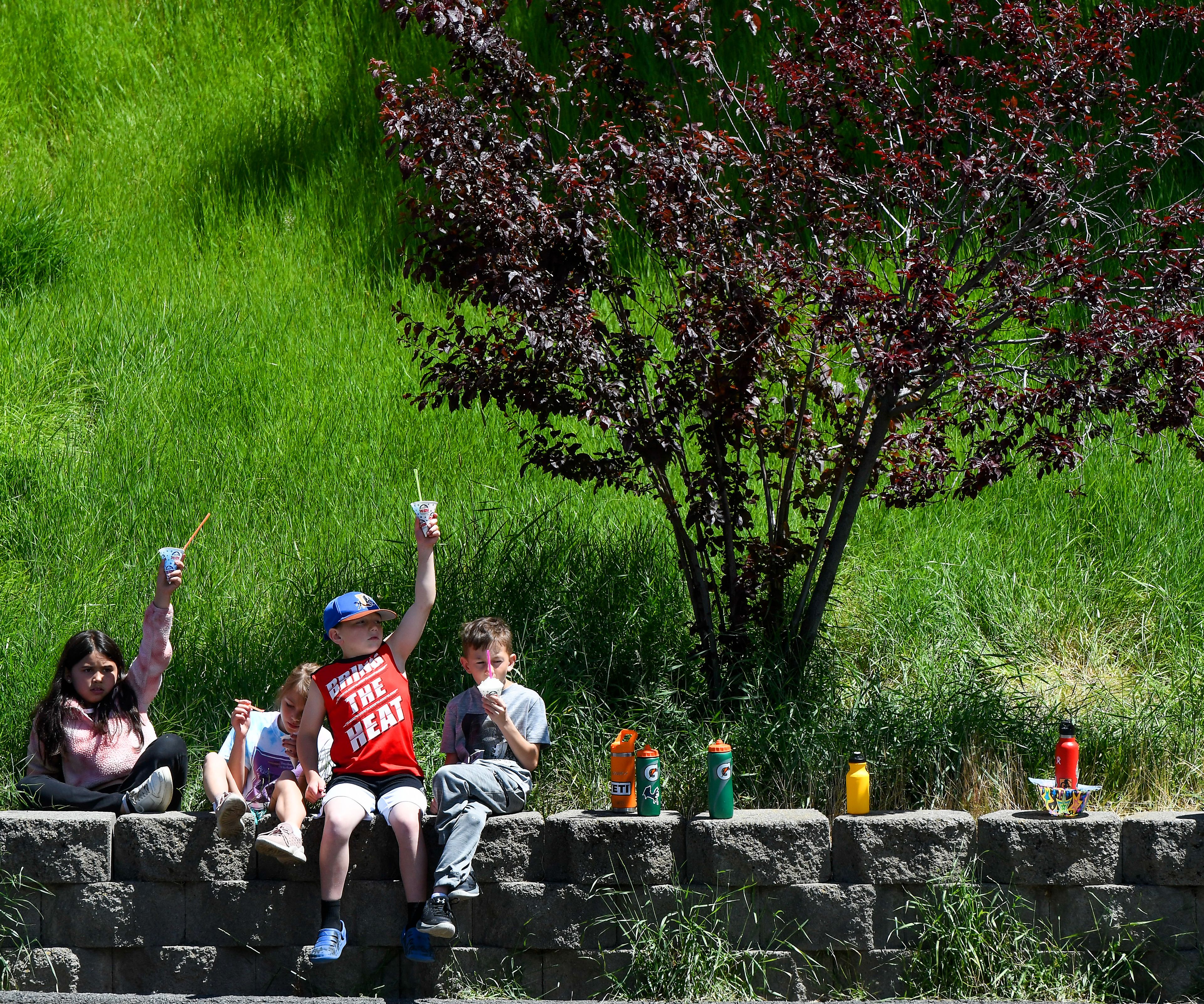 Zahara Allen, from left, Tess Duncan, Jarrod Anderson and Jase Baker, third-graders at Russell Elementary, raise their snow cones to the sky between bites of the treat at Asphalt Day on Wednesday.