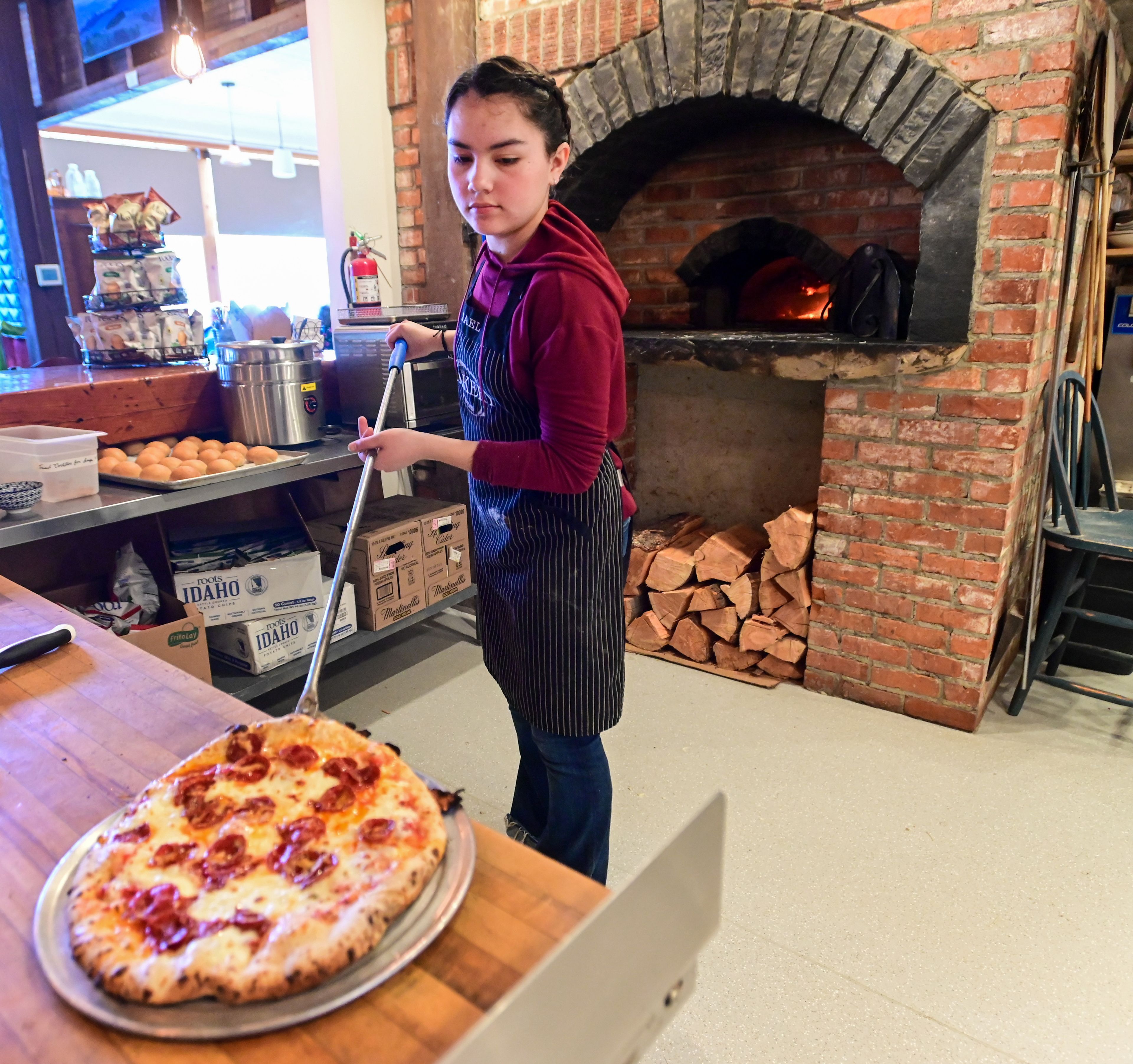 Pizza expediter Belle Orcutt, 15, removes a pepperoni pizza from the brick oven at The Pie Safe Bakery in Deary on Wednesday.