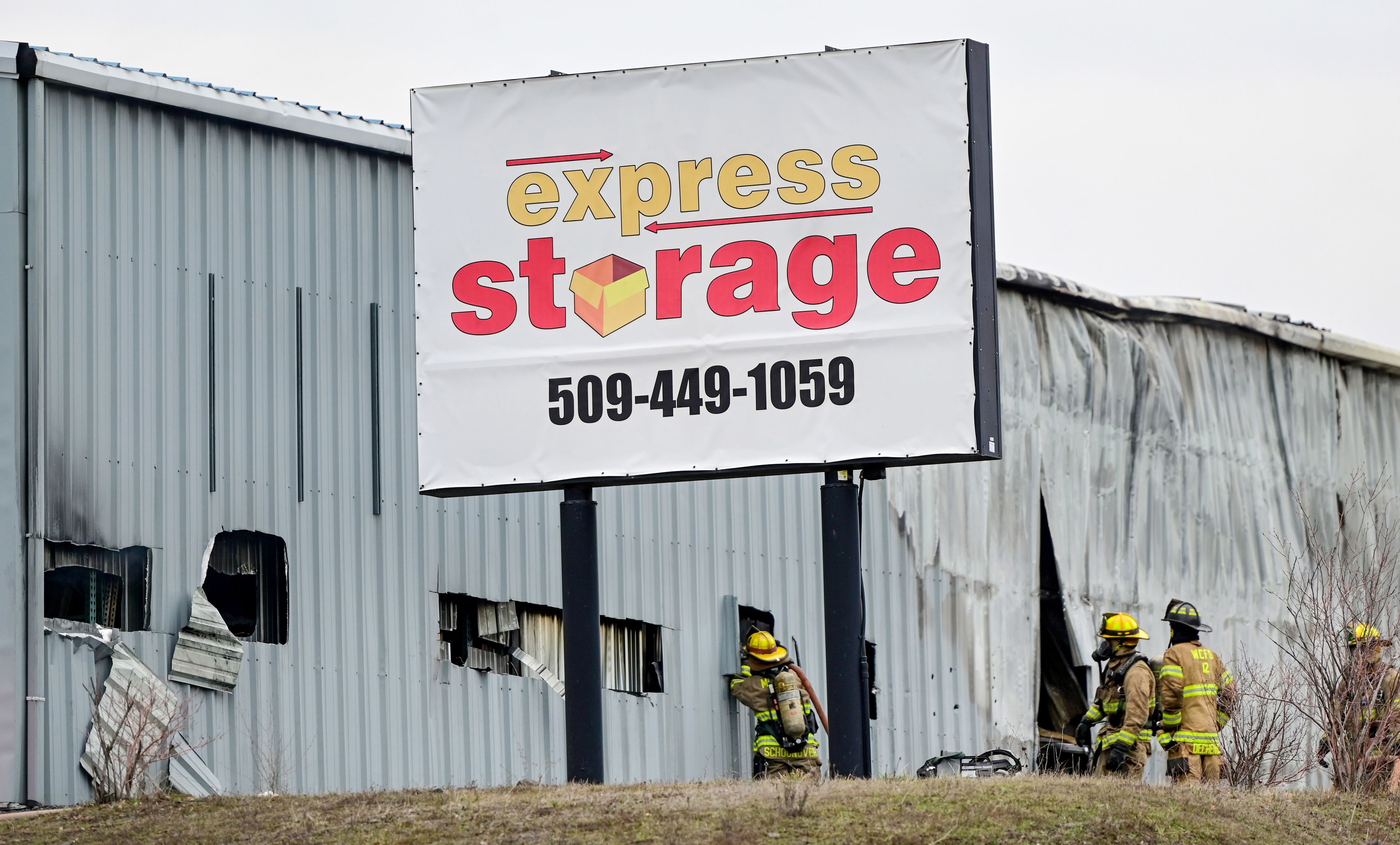 Fire crews spray through holes cut into the side of units at Express Storage in the aftermath of the large fire along Moscow-Pullman Highway on Thursday.