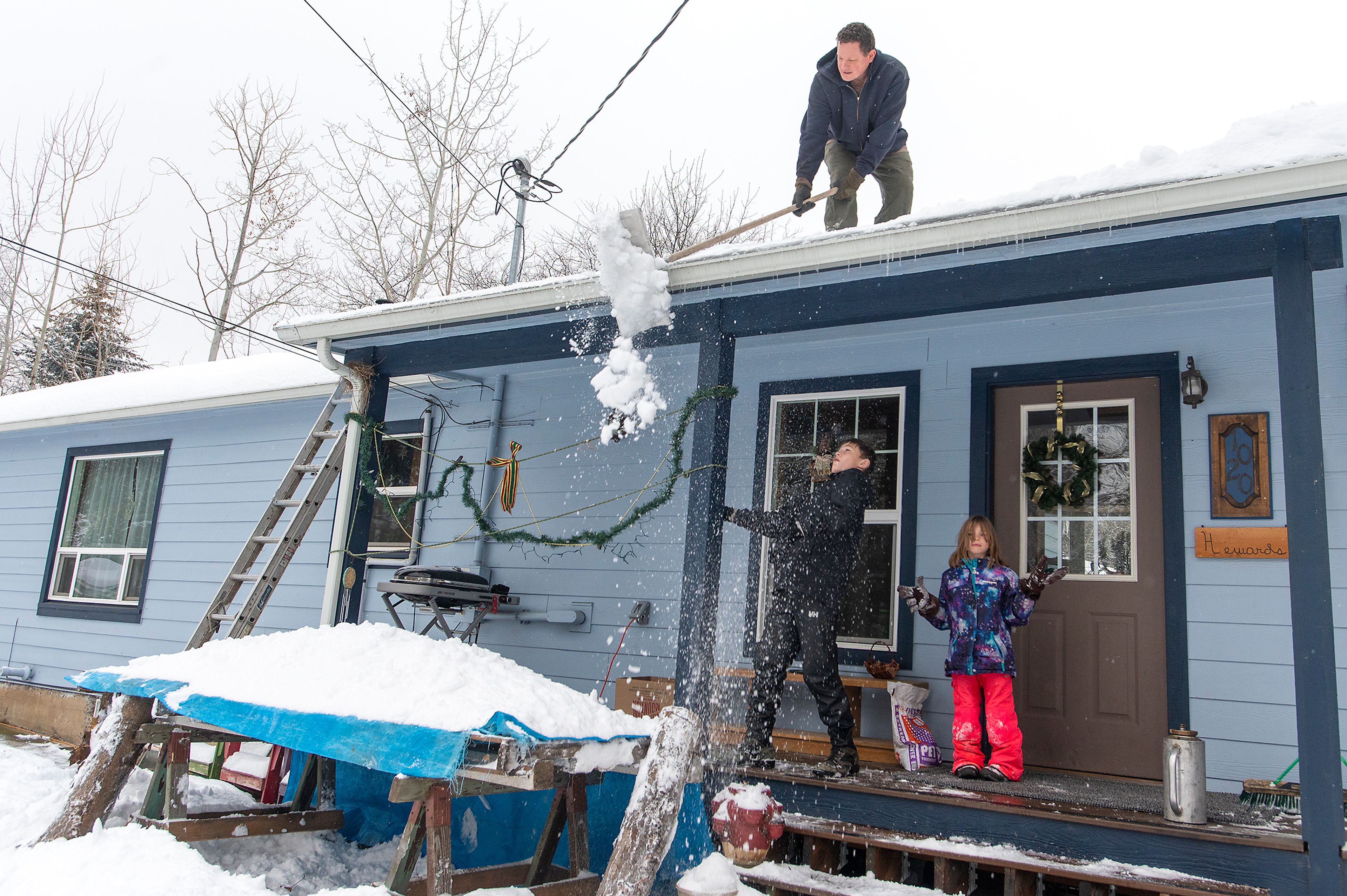 Michael Heward shovels snow from his roof onto a makeshift snow fort with his children, Tank, 12, left, and Luna, 6, Monday afternoon in Moscow.