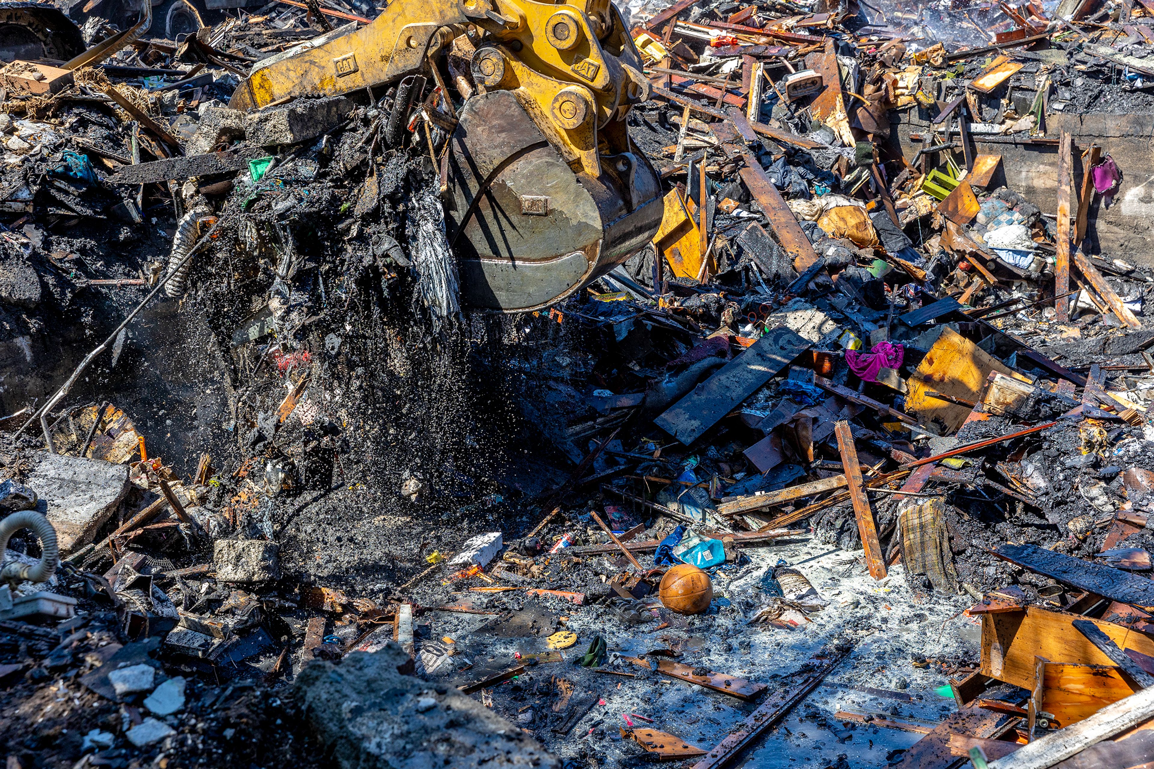 An excavators picks up debris so firefighters can put out any embers buried beneath the rubble at the scene of a structure fire Friday on Poplar Street in Clarkston.