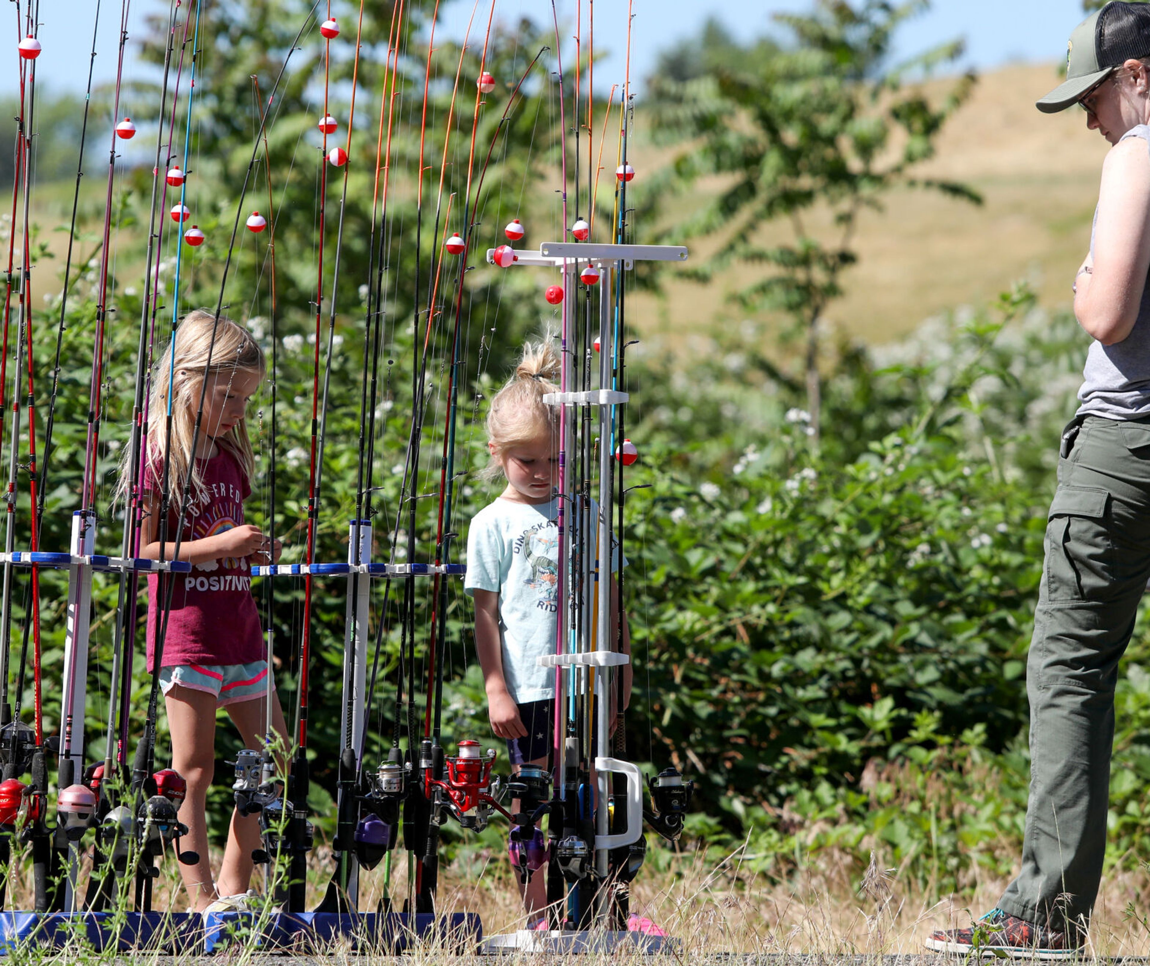 Evie Anders, 6, left, and Ivy Anders, 5, look at their fishing rod options with Rayanna Skalicky, right, an aquatic, hunting and trapping Education Technician with Idaho Fish and Game, at Kiwanis Park Pond during Idaho's Free Fishing Day on Saturday in Lewiston. The state entity offered free rods and other equipment to fishers for the day.