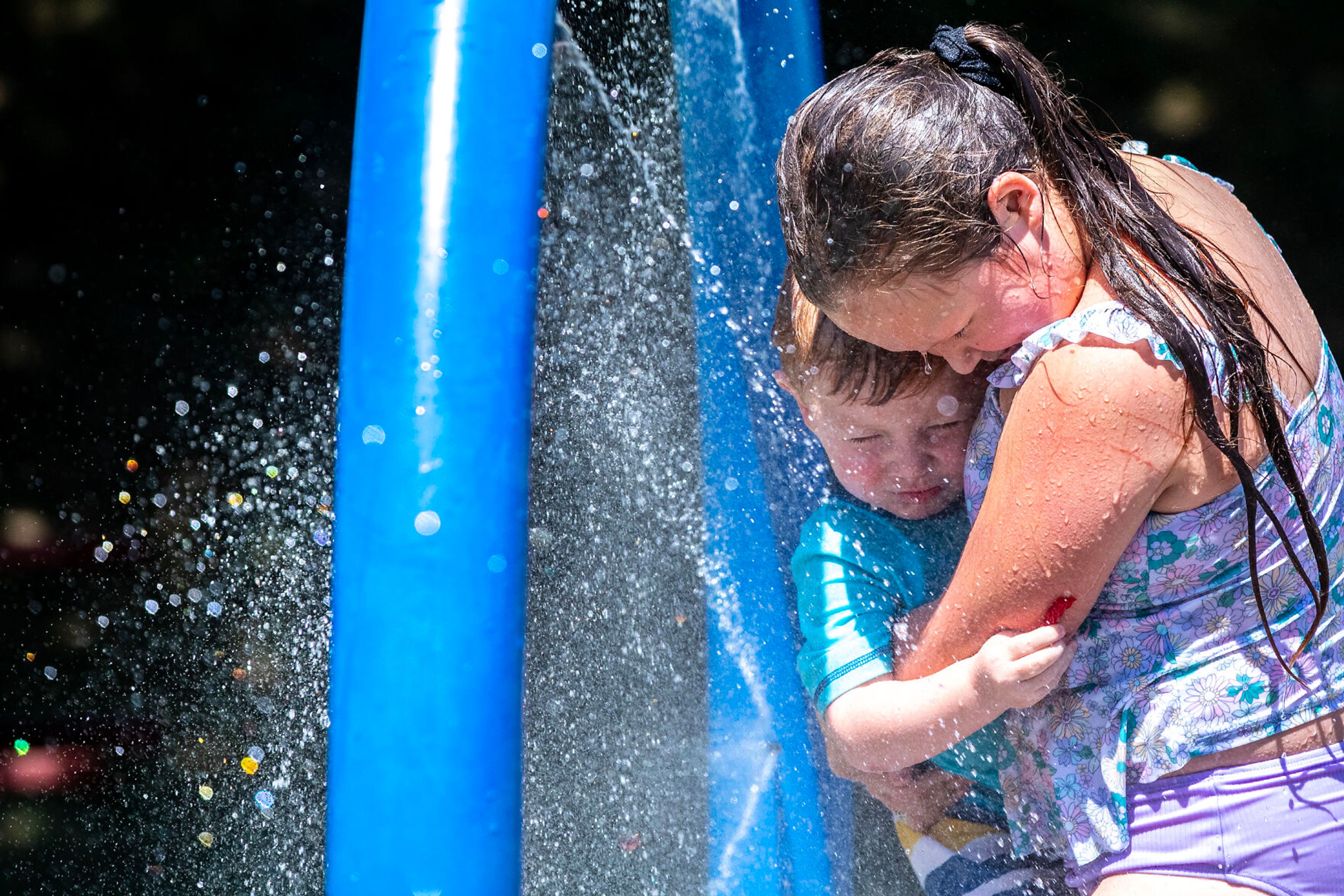 Kaydence Dammerman, 9, holds her brother Raxton Dammerman, 2 1/2, as they run through the splash pad Friday, July 28, at the Orofino City Park splash pad.