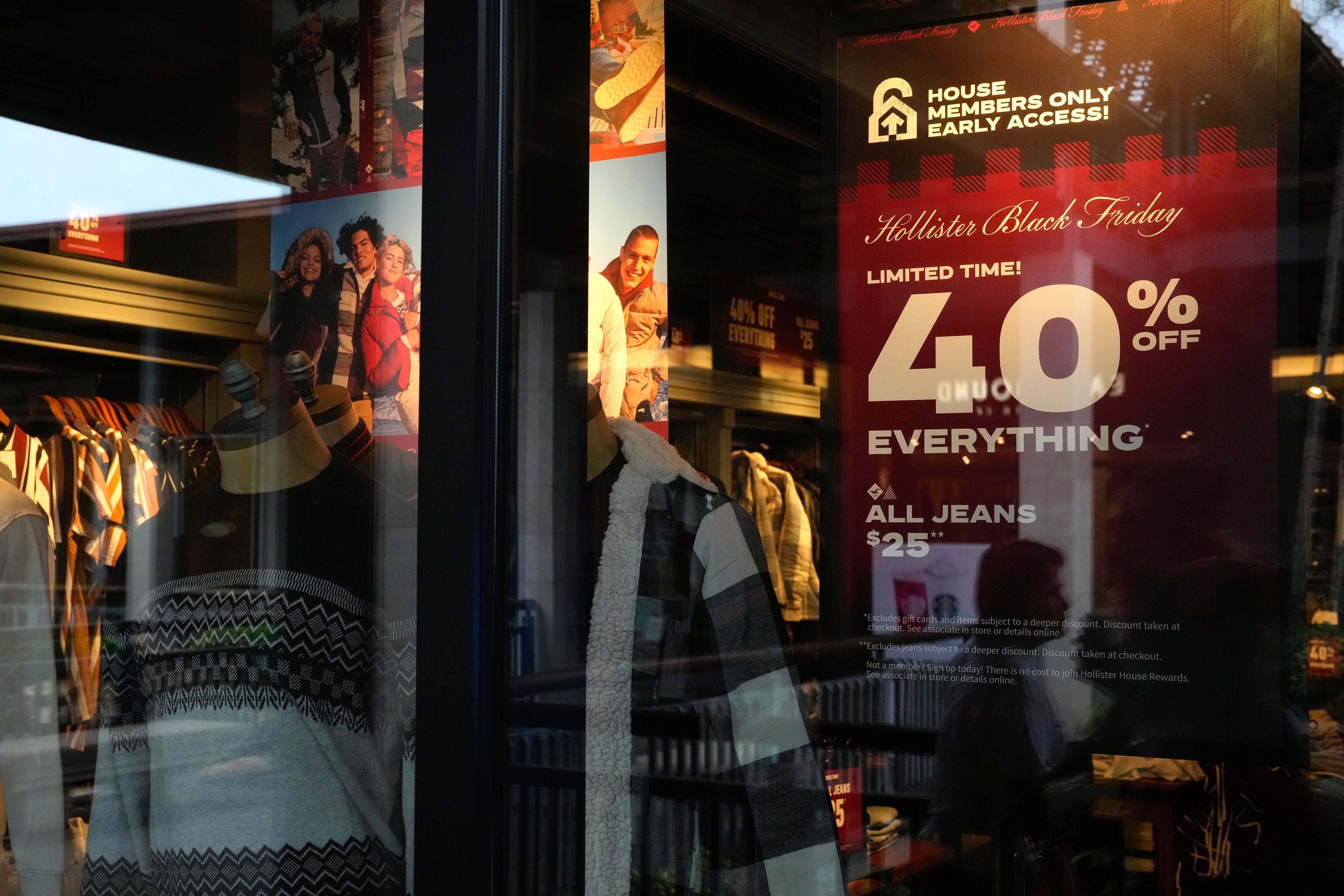 The reflections of passing shoppers are seen in the glass of a Hollister clothing store advertising sales, ahead of Black Friday and the Thanksgiving holiday, Monday, Nov. 21, 2022, in Miami. Retailers are ushering in the start of the holiday shopping season on the day after Thanksgiving, preparing for the biggest crowds since 2019. (AP Photo/Rebecca Blackwell)