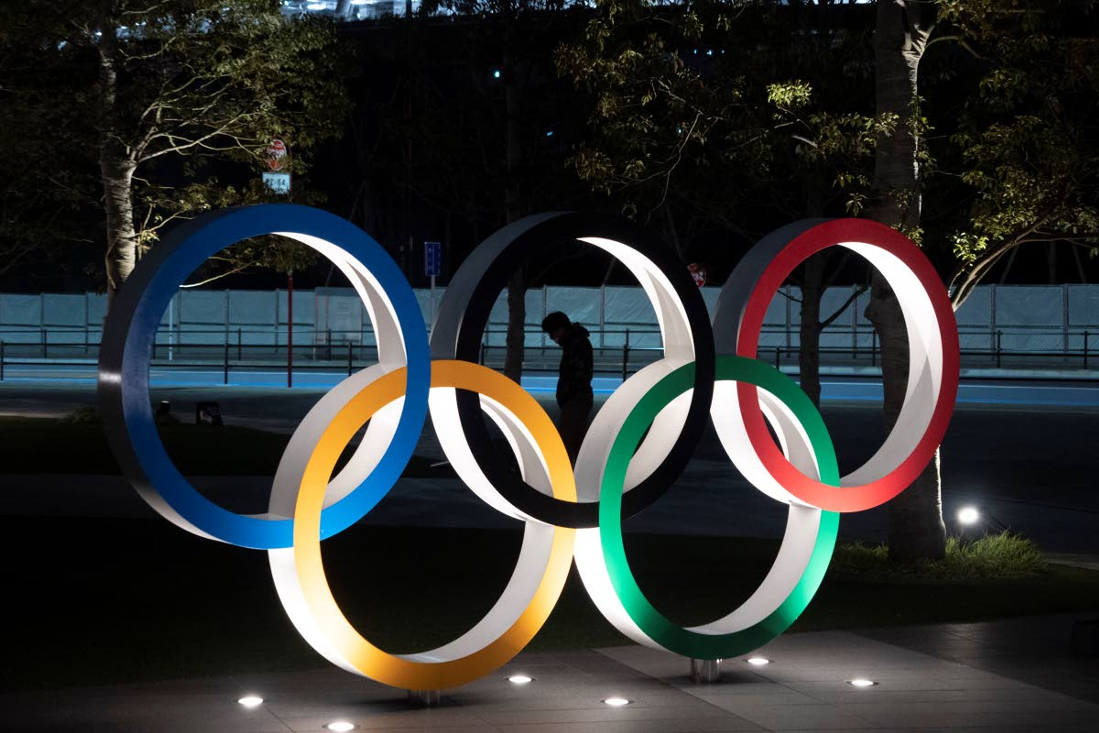 FILE - In this March 24, 2020, a man is seen through the Olympic rings in front of the New National Stadium in Tokyo. IOC officials say the Tokyo Olympics will open on July 23 and almost nothing now can stop the games from going forward. (AP Photo/Jae C. Hong, File)