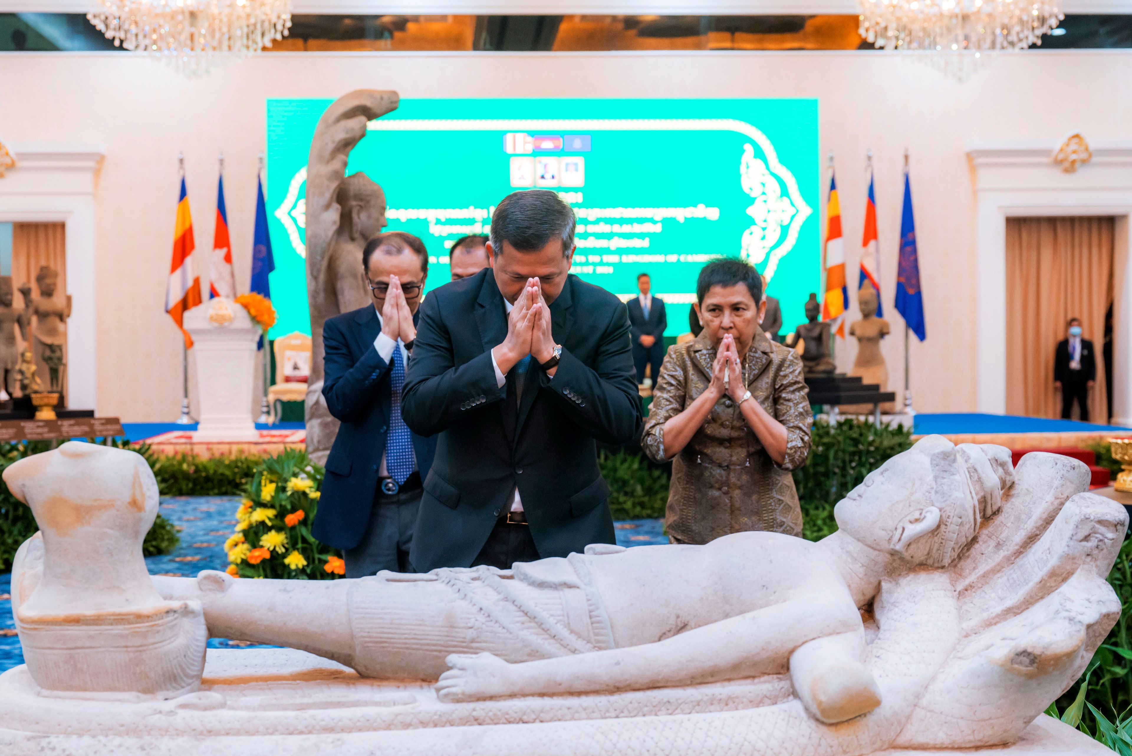 In this photo released by Agence Kampuchea Press (AKP), Cambodian Prime Minister Hun Manet, front, prays before a statue with Culture and Fine Arts Phoeurng Sackona, right, during a ceremony for the return of artifacts in Peace Palace in Phnom Penh, Cambodia, Thursday, Aug. 22, 2024. (AKP via AP)