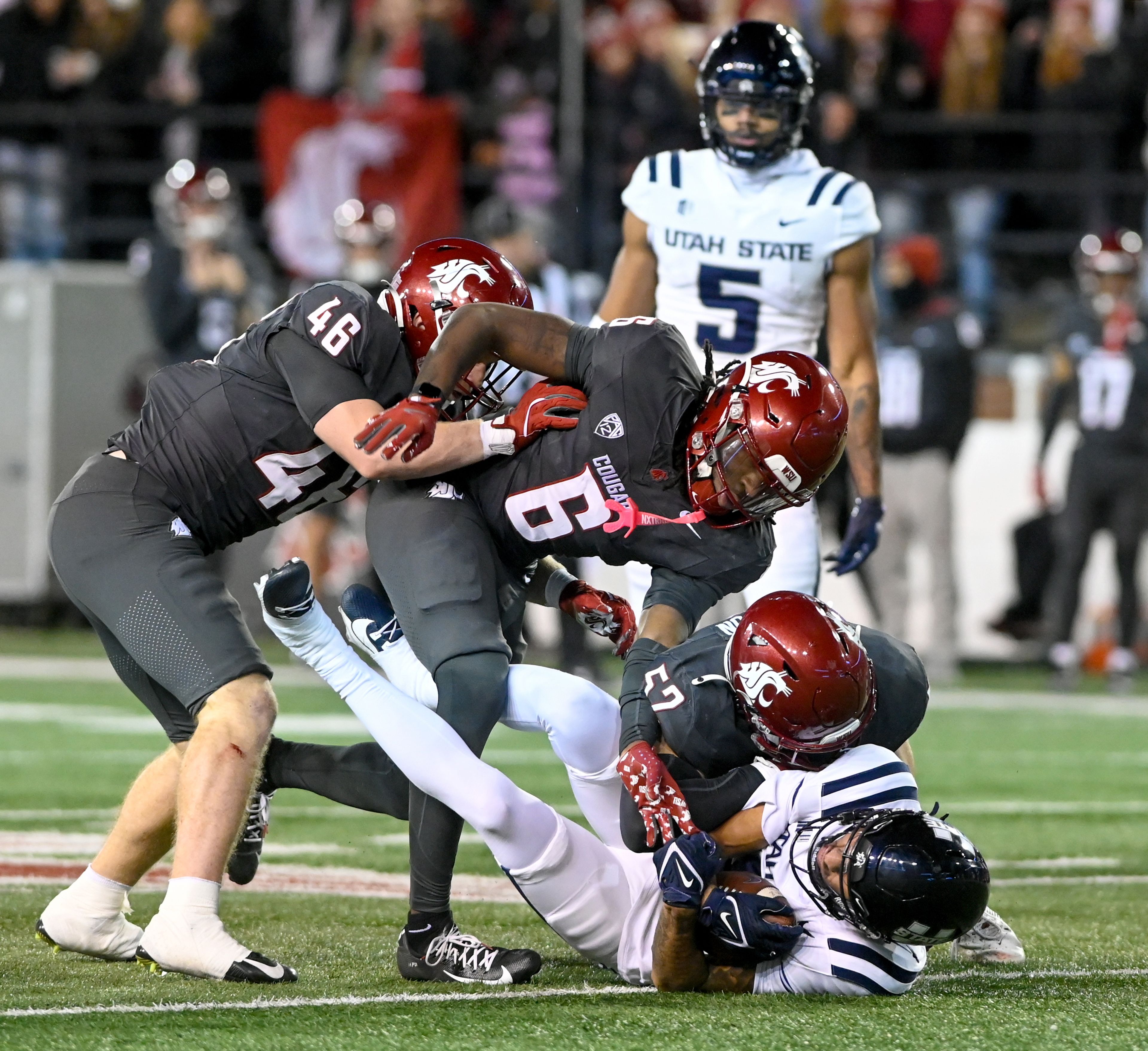 Washington State linebacker Parker McKenna (46), Washington State defensive back Adrian Wilson (6) and Washington State linebacker Kyle Thornton (52) tackle Utah State wide receiver Grant Page (8) Saturday at Gesa Field in Pullman.