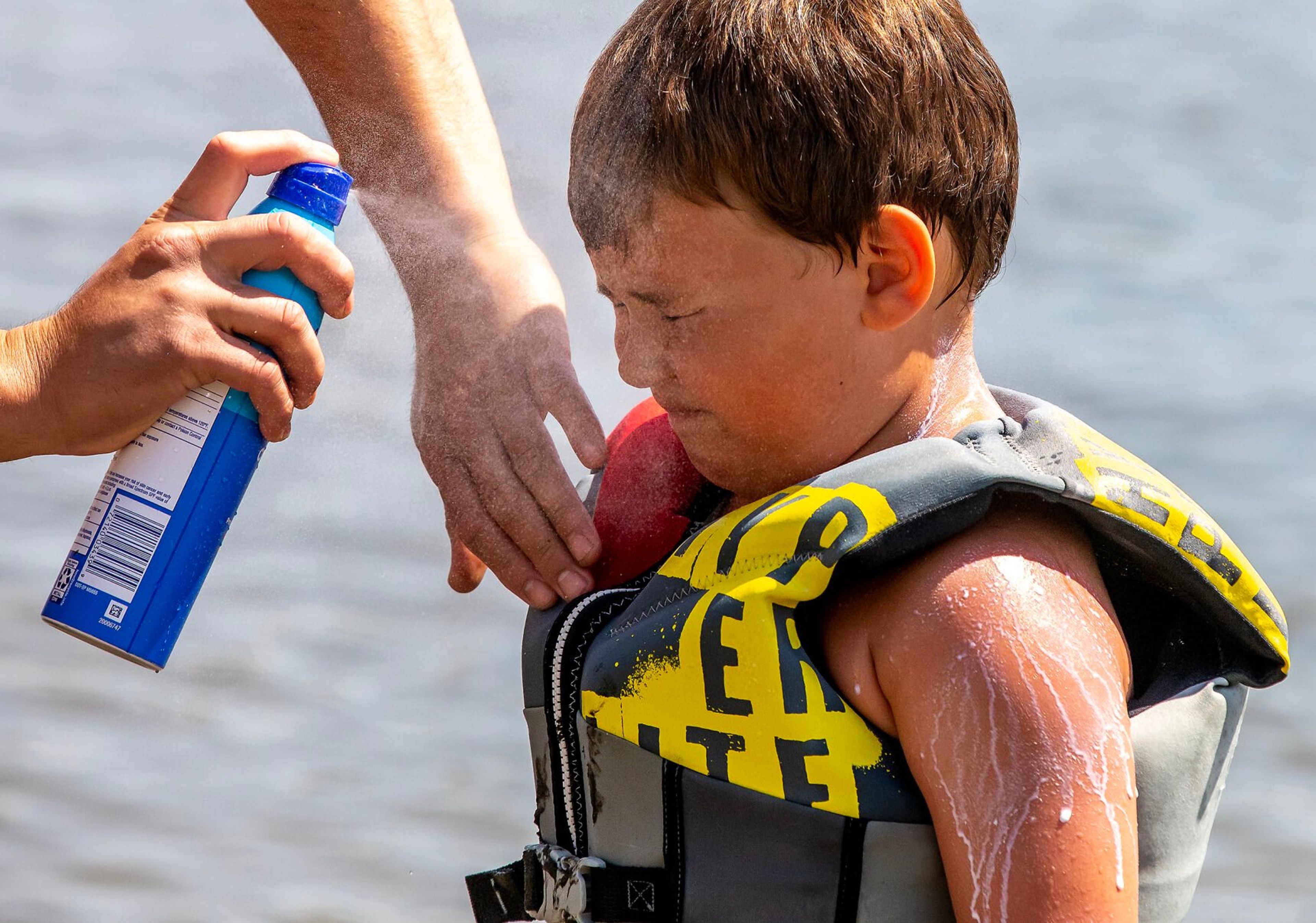 Billy Stevenson sprays down Braxton Stevenson, 5, with sun screen as they play at Chestnut Beach Wednesday, June 7, in Clarkston.