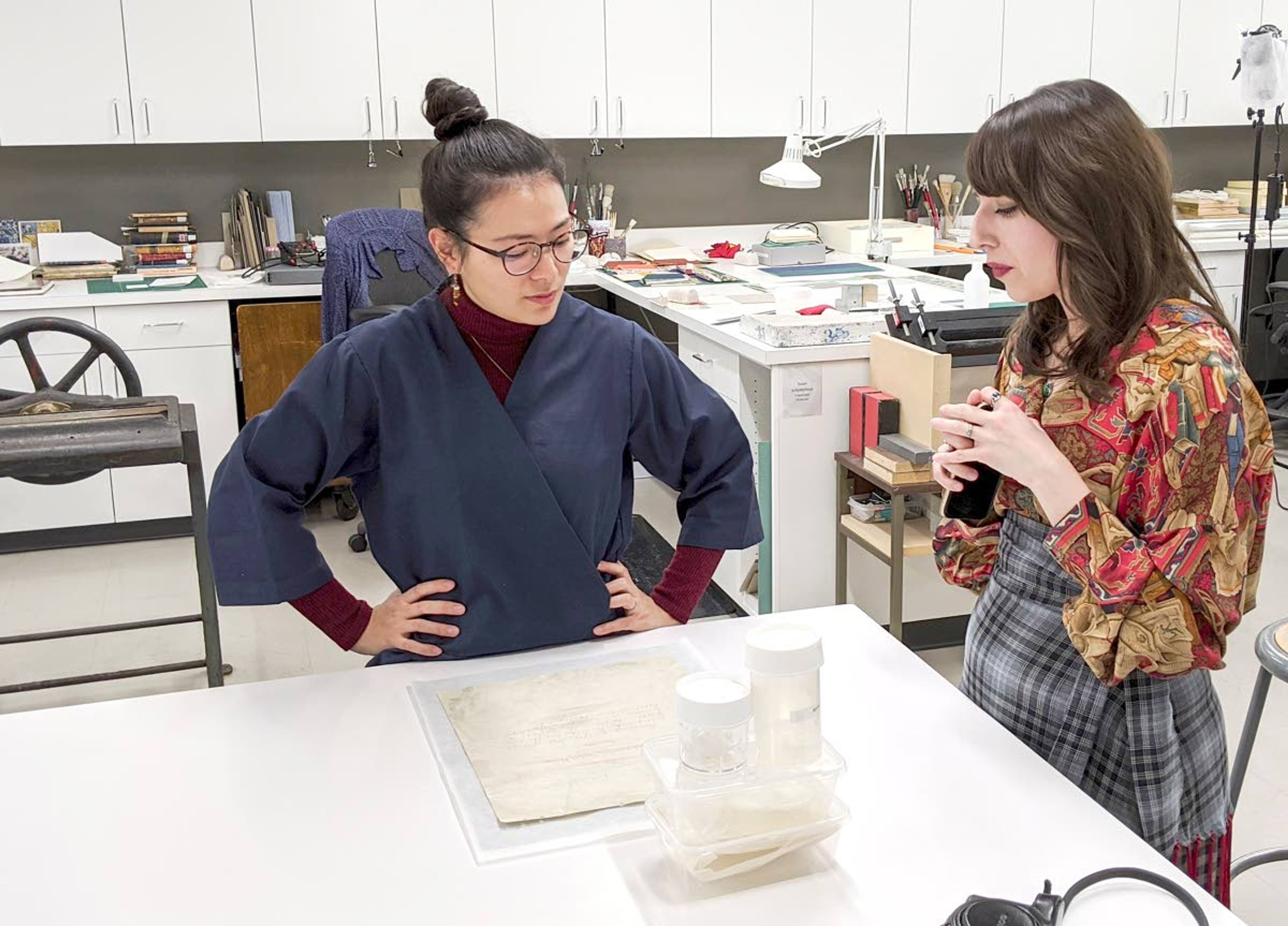 University of Utah Paper Conservator Stacey M. Kelly (left) and Idaho State Archives Collections Archivist Layce Johnson study the first page of the Idaho Constitution in December 2019. The plastic containers hold the pieces of lamination that came off the page.