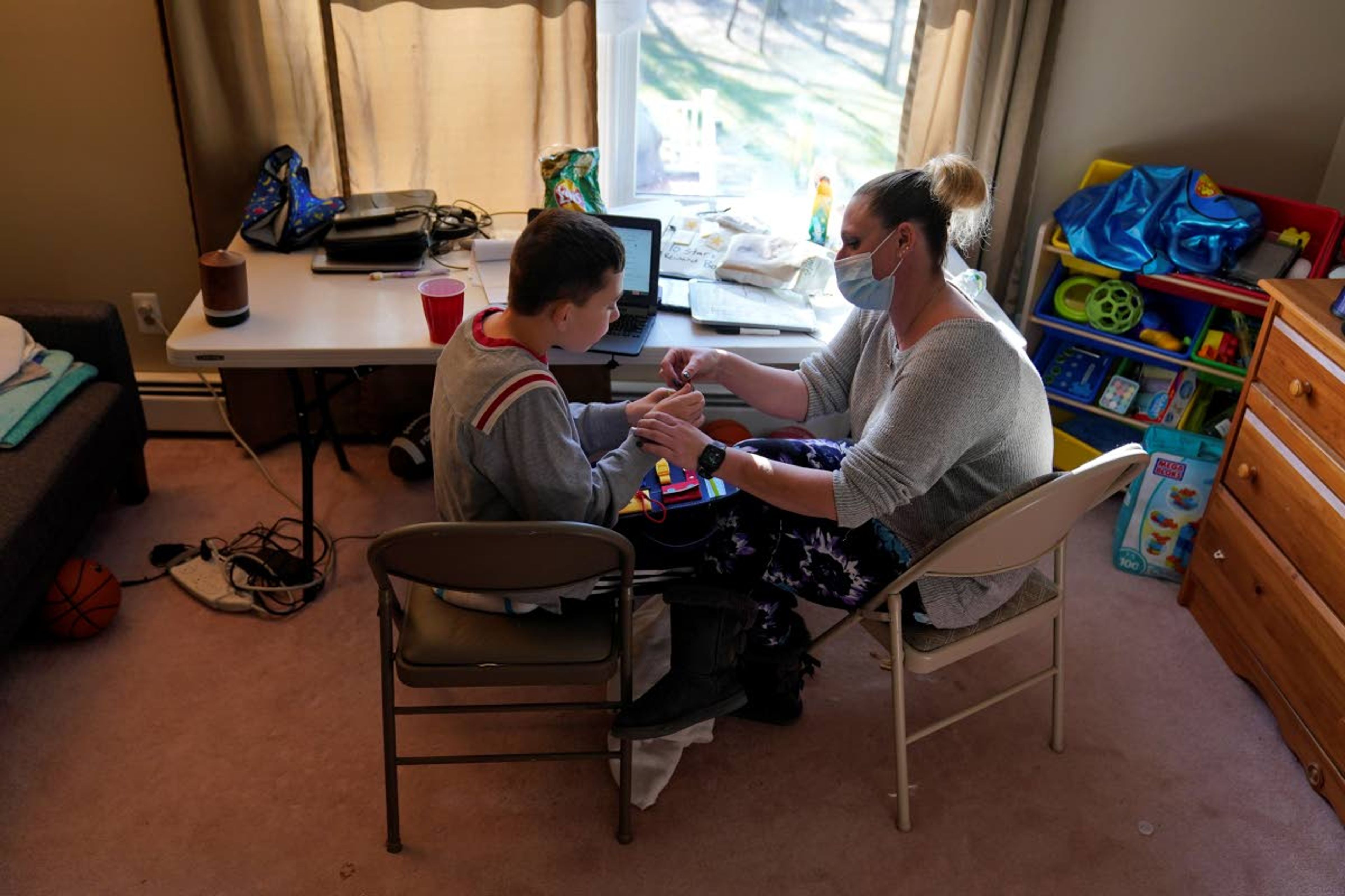 Paraprofessional Jessica Wein helps Josh Nazzaro stay focussed while attending class virtually from his home in Wharton, N.J., Wednesday, Nov. 18, 2020. Without any in-school special education services for months, Nazzaro’s normally sweet demeanor has sometimes given way to aggressive meltdowns that had been under control before the pandemic. The teenager, who has autism and is nonverbal, often wanted no part of his online group speech therapy sessions, and when he did participate, he needed constant hands-on guidance from aides hired by his family. (AP Photo/Seth Wenig)