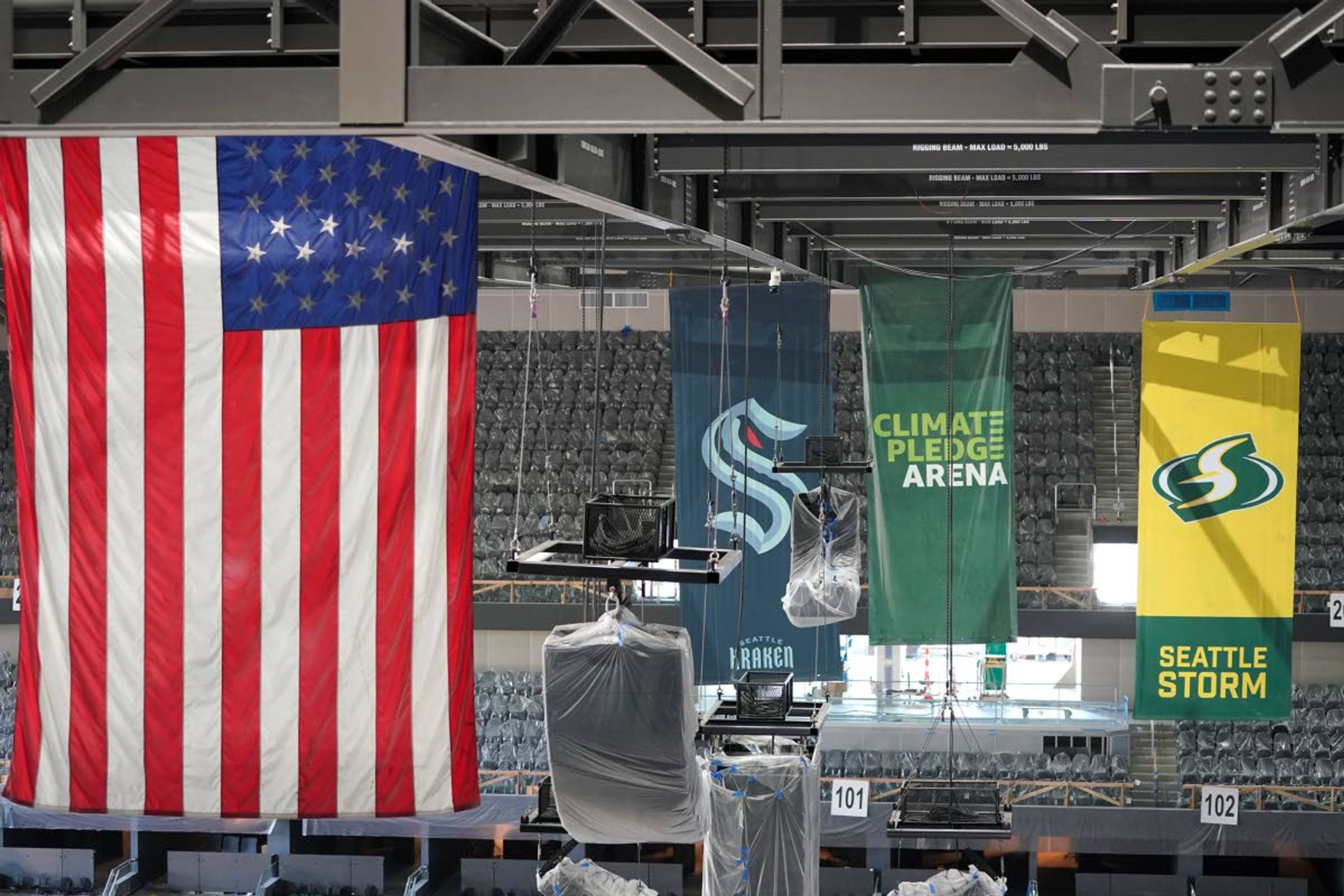 United States and team flags hang in the rafters of the Climate Pledge Arena during a media tour of the facility, Monday, July 12, 2021, in Seattle. The arena will be the home of the NHL hockey team Seattle Kraken and the WNBA Seattle Storm basketball team as well as hosting concerts and other performing arts events. (AP Photo/Ted S. Warren)