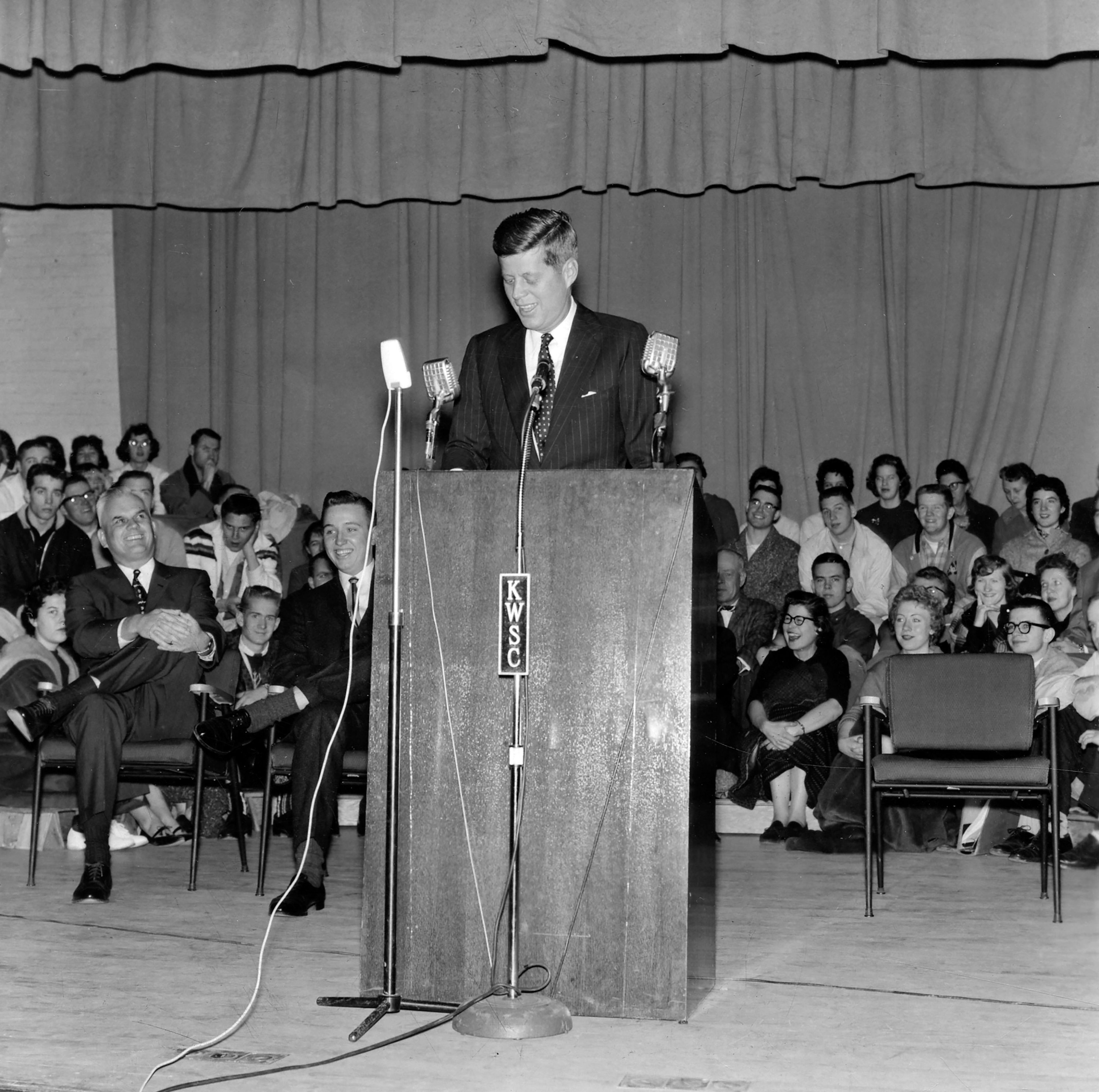 Presidential candidate John F. Kennedy speaks on stage in Bryan Hall on the Washington State University campus in Pullman. So many students tried to attended that they seated them on the stage behind him.