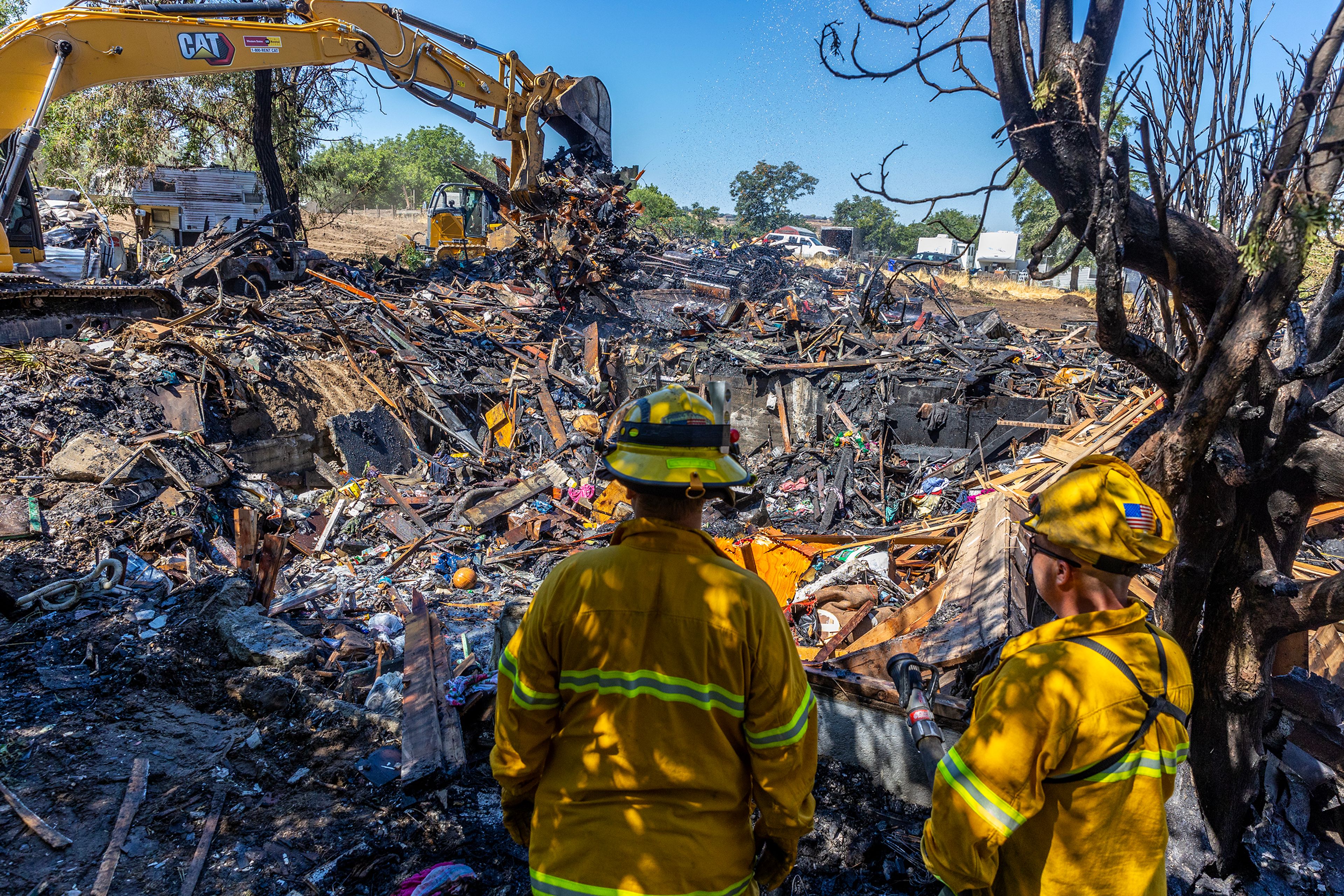 Firefighters look on as an excavators moves debris at the scene of a structure fire caused by a firework on Friday in Clarkston.