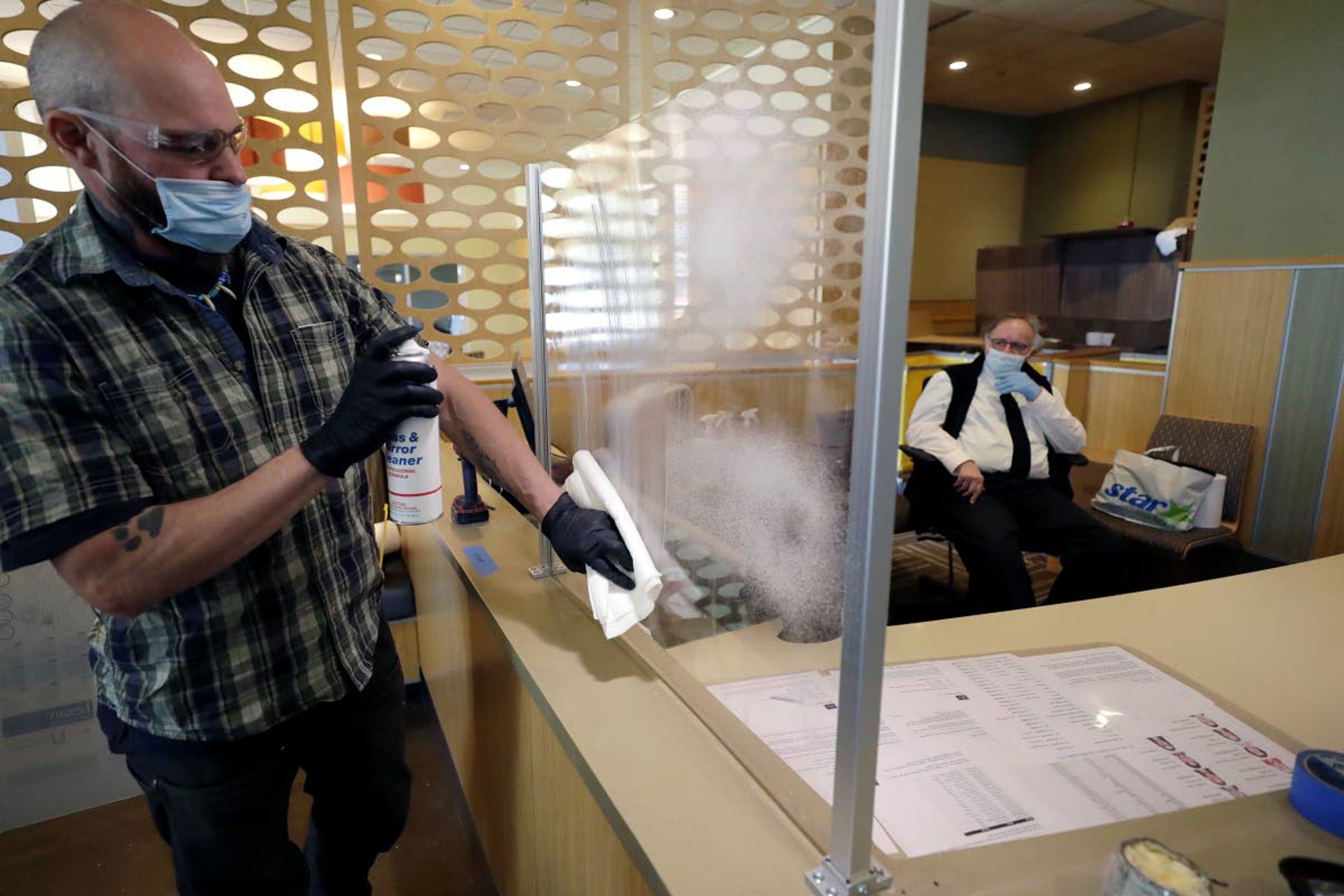 Glass installer Michael Cane, of Burlington, Mass., left, cleans a newly installed plastic barrier Thursday, May 21, 2020, at a security desk at the entrance to a dormitory, at Boston University, in Boston. Boston University is among a growing number of universities making plans to bring students back to campus this fall, but with new measures meant to keep the coronavirus at bay. (AP Photo/Steven Senne)