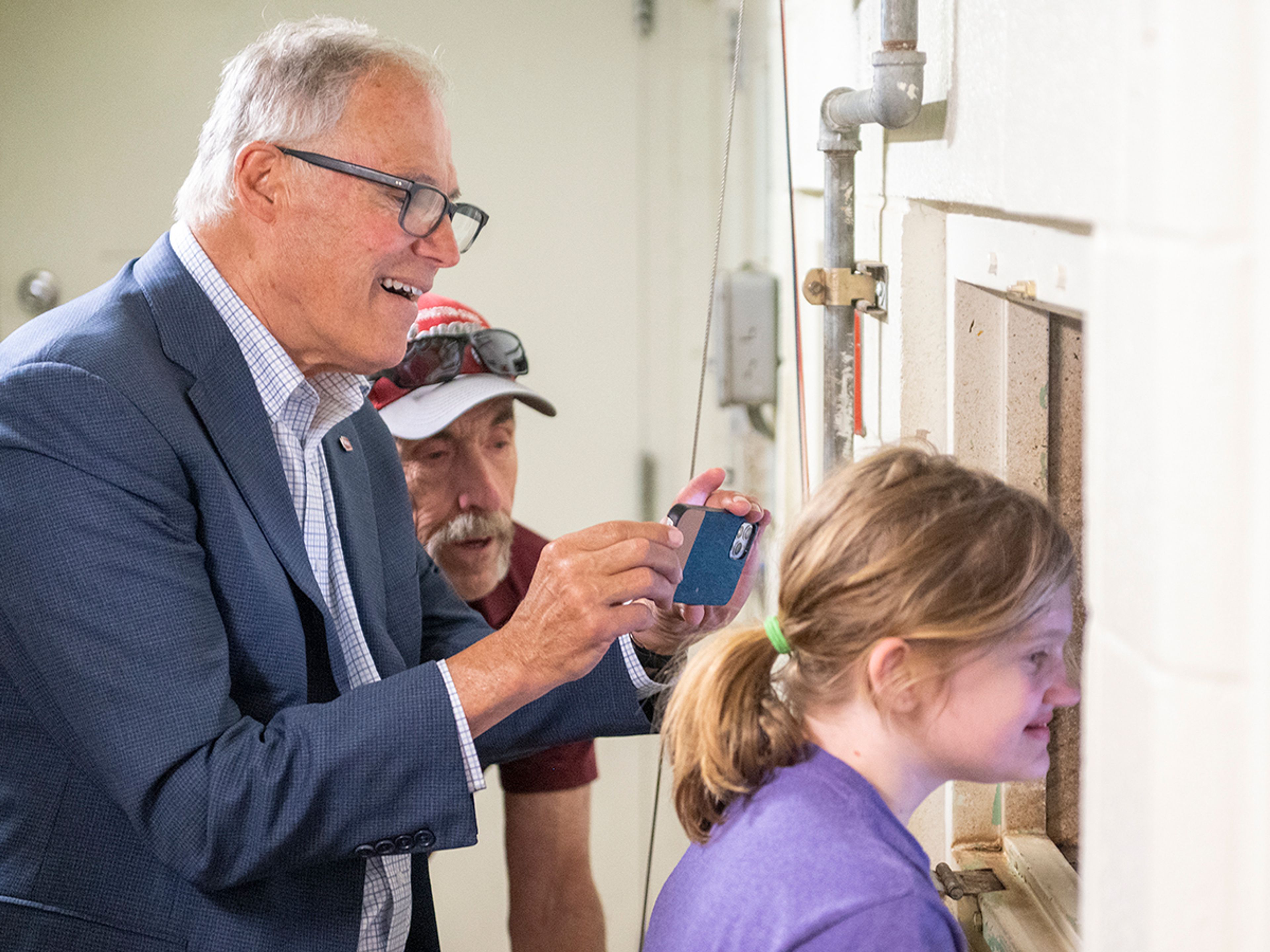 Washington Gov. Jay Inslee takes photos as his granddaughter peeks through a window to see grizzly bears while touring Washington State University’s Bear Center on Thursday afternoon in Pullman.