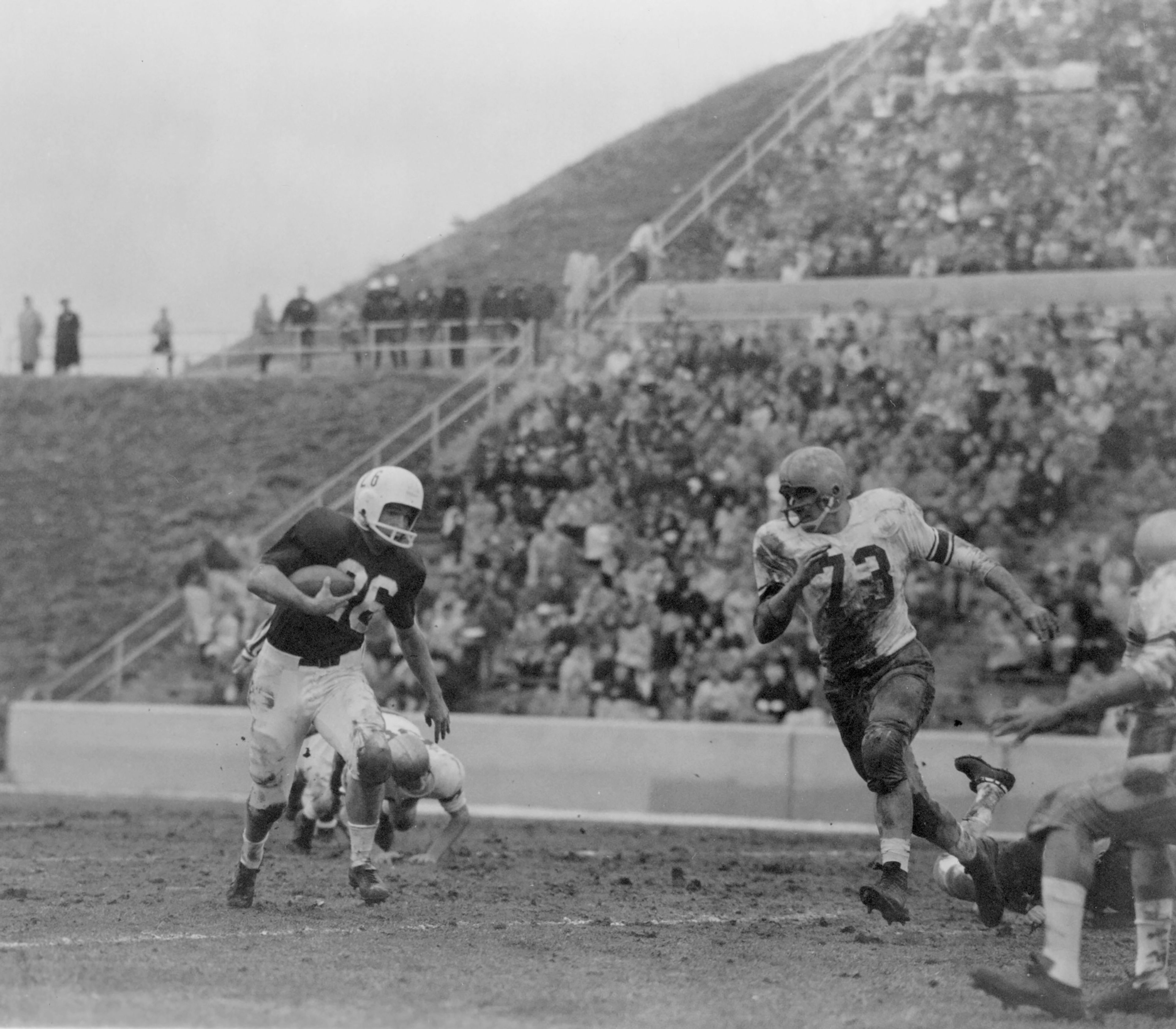 Bob White (73) of the University of Washington chases after fullback Carl Ketchie (26) of Washington State University in their final Pacific Coast Conference game; the Cougars beat the Huskies 18-14 in Spokane. Unfortunately, University of California edged Stanford University 16-15 in a game ending just minutes later, and Cal took that Rose Bowl spot from WSU.