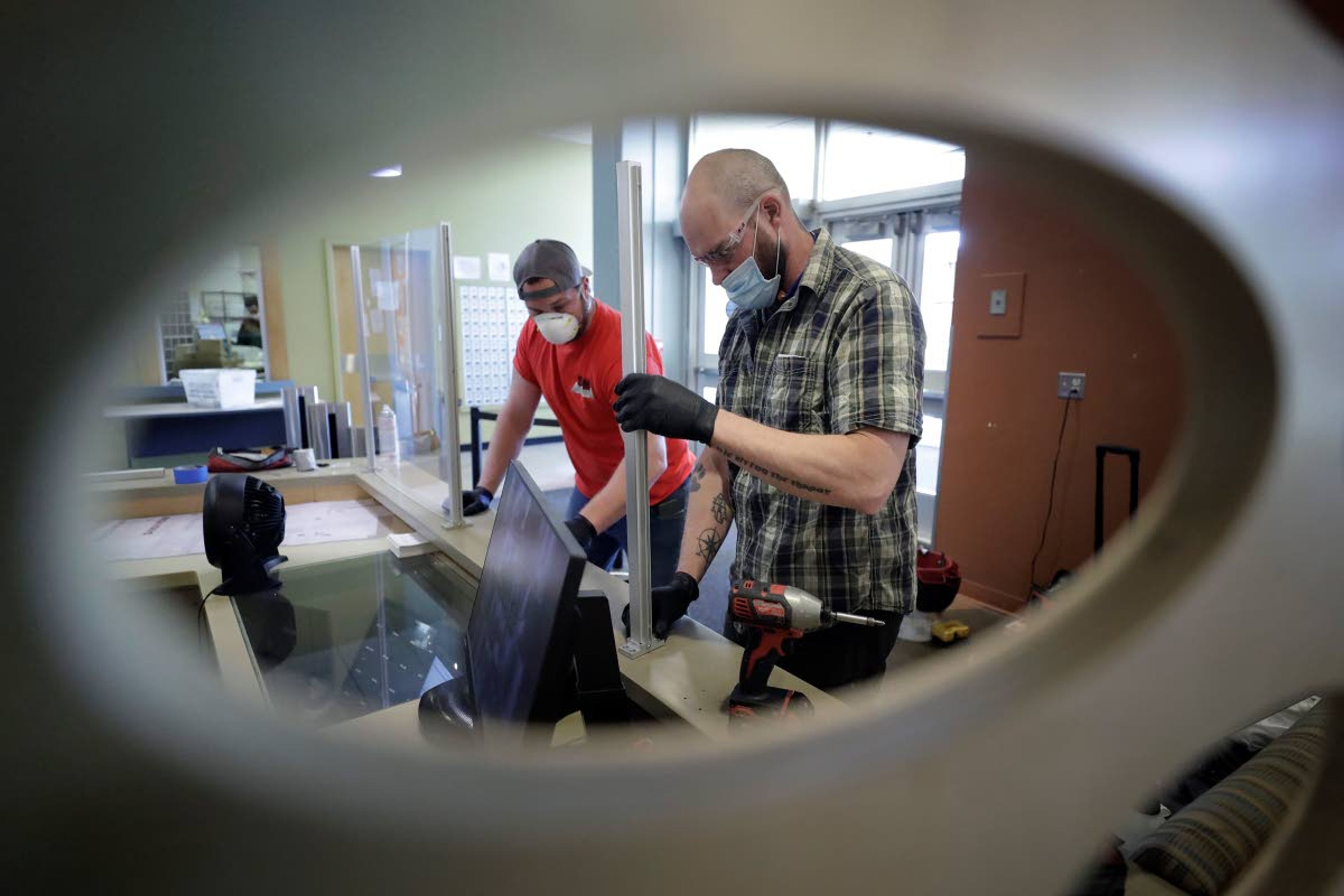 Glass installers Nick Trueblood, of Clinton, Mass., left, and Michael Cane, of Burlington, Mass., right, install a plastic barrier, Thursday, May 21, 2020, at a security desk at the entrance to a dormitory, at Boston University, in Boston. Boston University is among a growing number of universities making plans to bring students back to campus this fall, but with new measures meant to keep the coronavirus at bay. (AP Photo/Steven Senne)