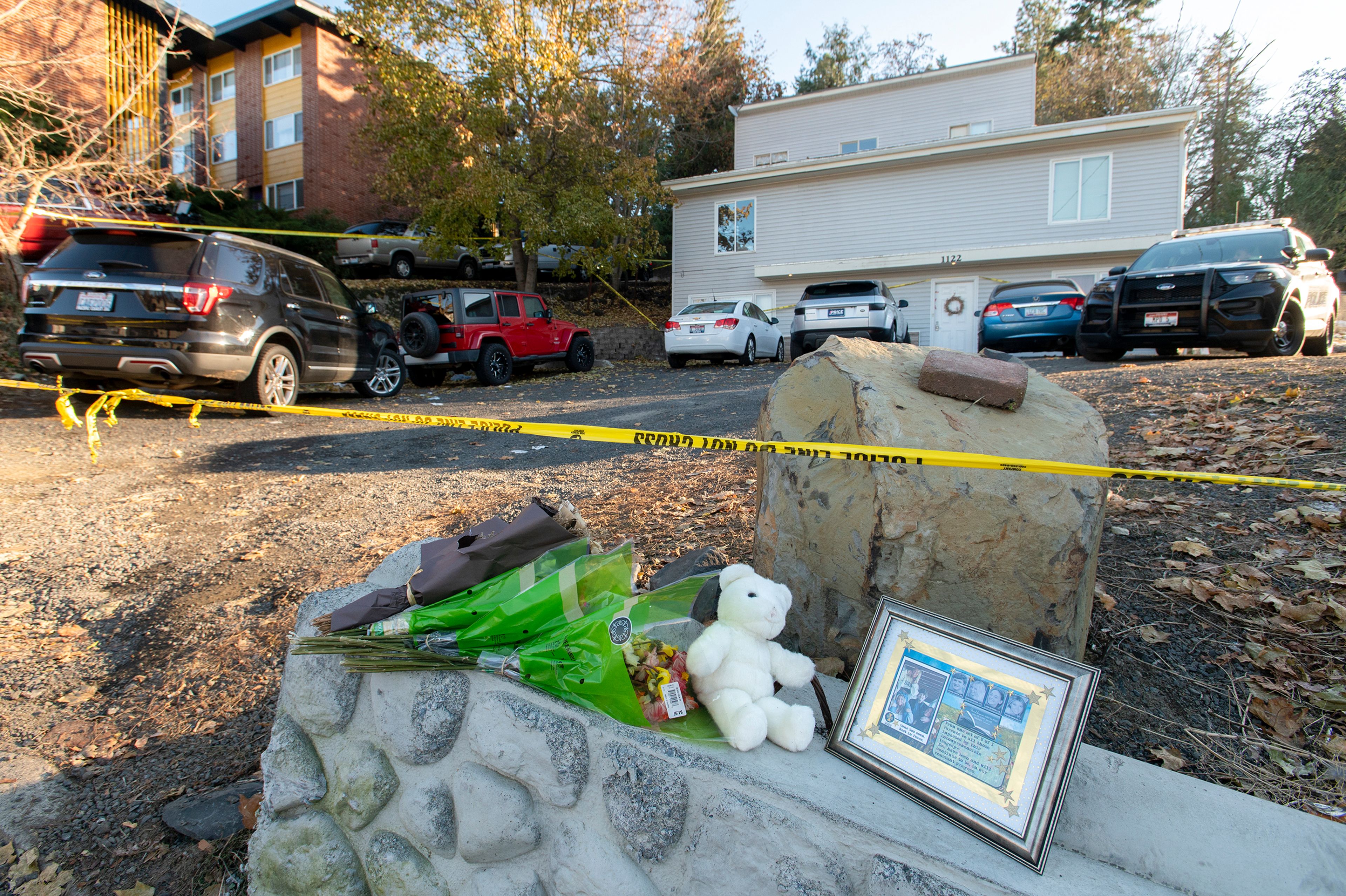 A framed picture of the four University of Idaho students slain in a quadruple homicide rests next to a teddy bear and bouquets of flowers Monday outside the crime scene on King Road in Moscow.