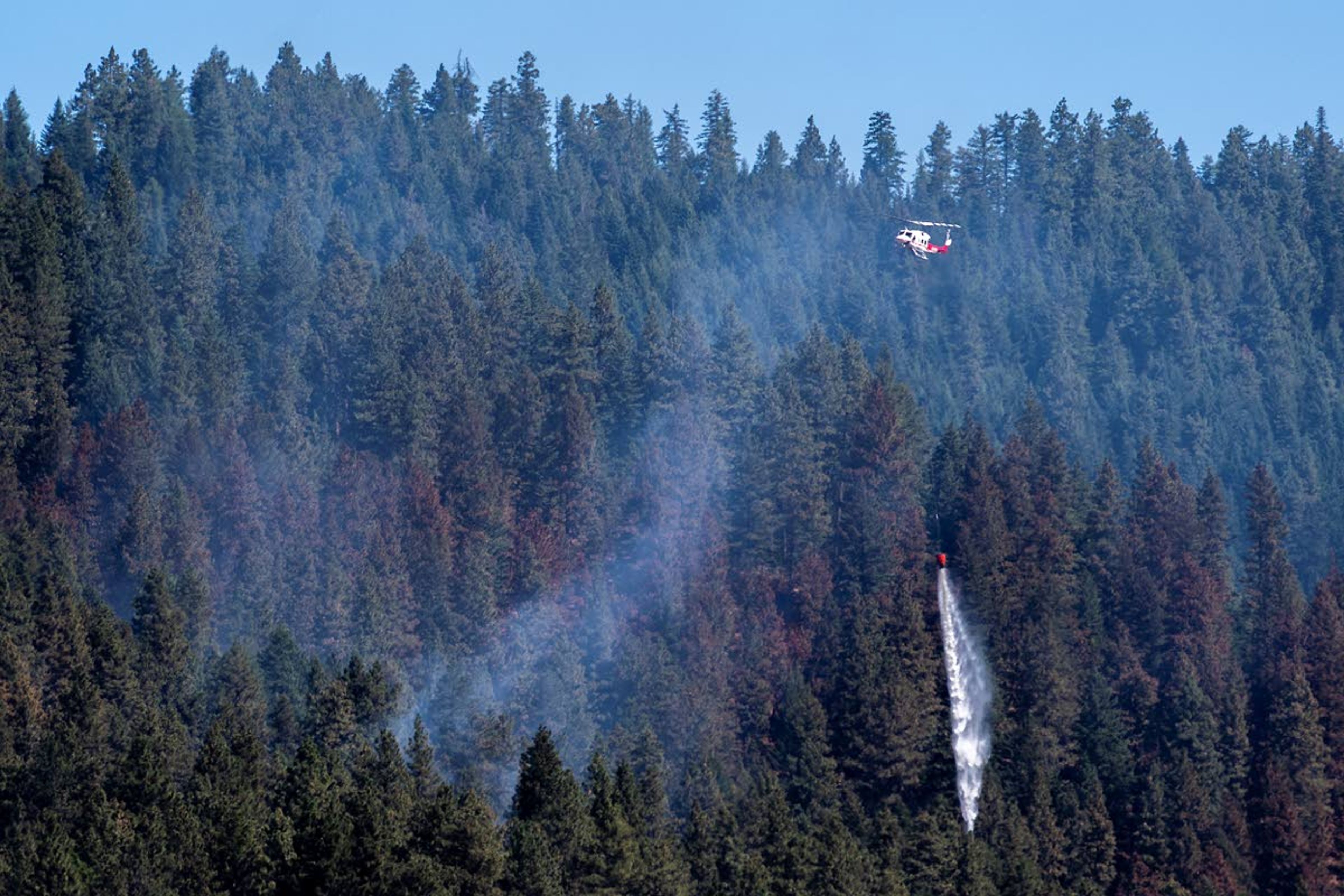 A helicopter drops a bucket of water near the remaining flames of a wildfire along Idlers Rest Road and West Twin Road on Tuesday in Moscow.