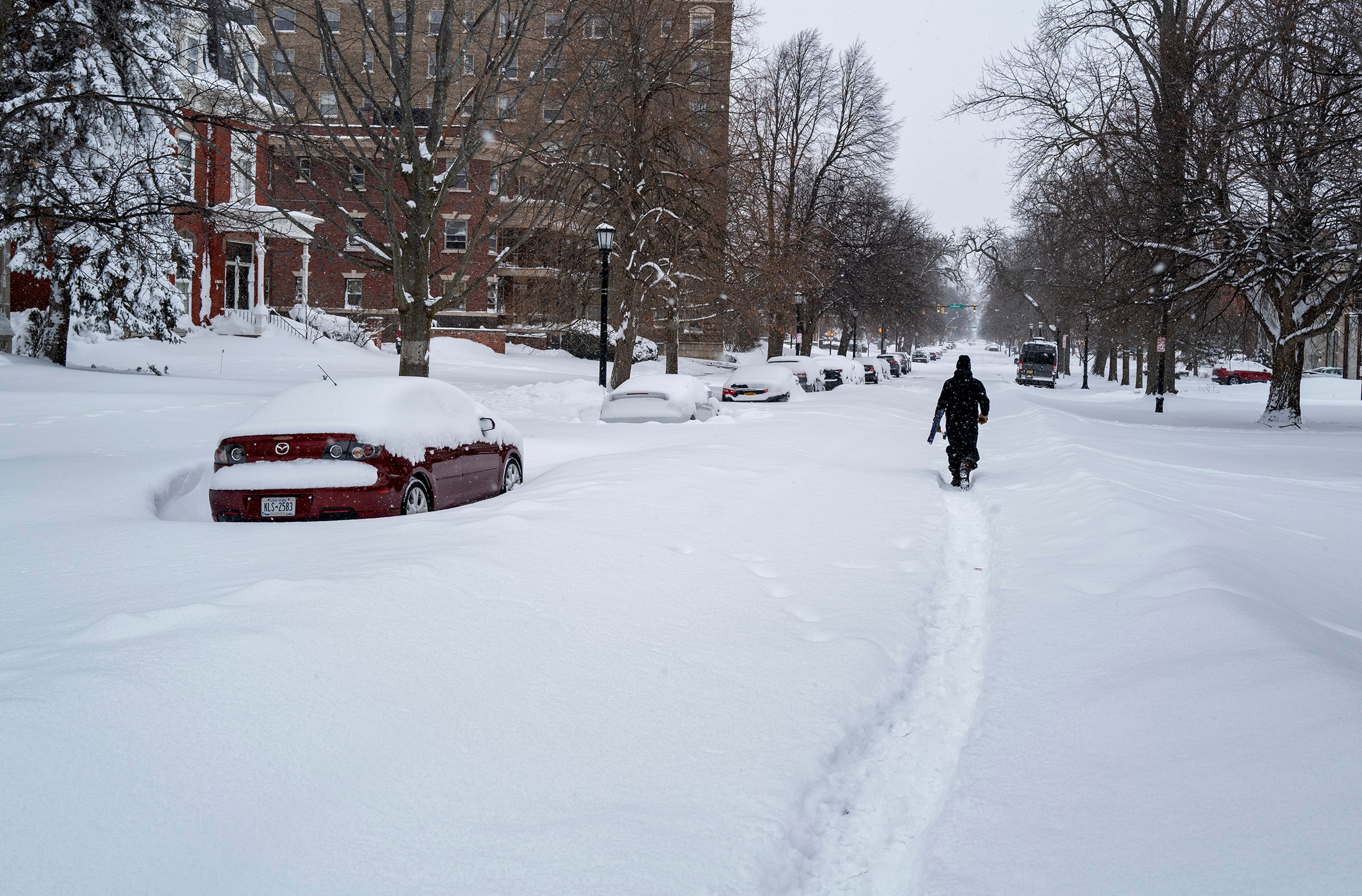 Daniel Shafer of Buffalo, N.Y., walks along a path in the street in the Elmwood Village neighborhood of Buffalo, Monday, Dec. 26, 2022, after a massive snow storm blanketed the city. Along with drifts and travel bans, many streets were impassible due to abandoned vehicles. (AP Photo/Craig Ruttle)