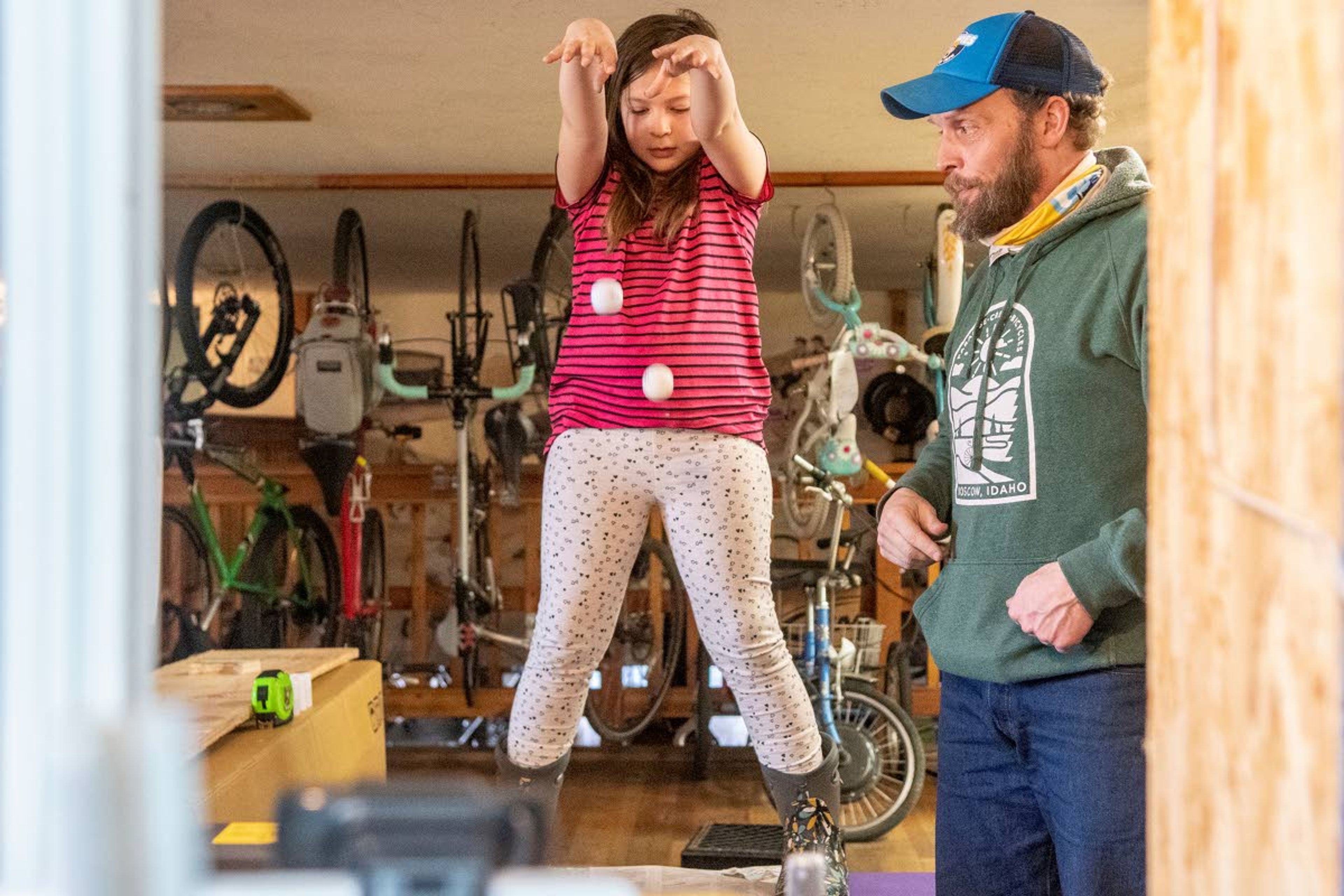 Zach Wilkinson/Daily NewsT. Jay Clevenger, owner of Paradise Creek Bicycles, teaches Science on Ice program virtually with the help of his daughter, Sandra, 8, who he nicknamed “Samboni” in reference to a Zamboni used at ice rinks. Sandra is seen dropping a golf ball and pingpong ball above a newspaper as they teach students about momentum and mass.