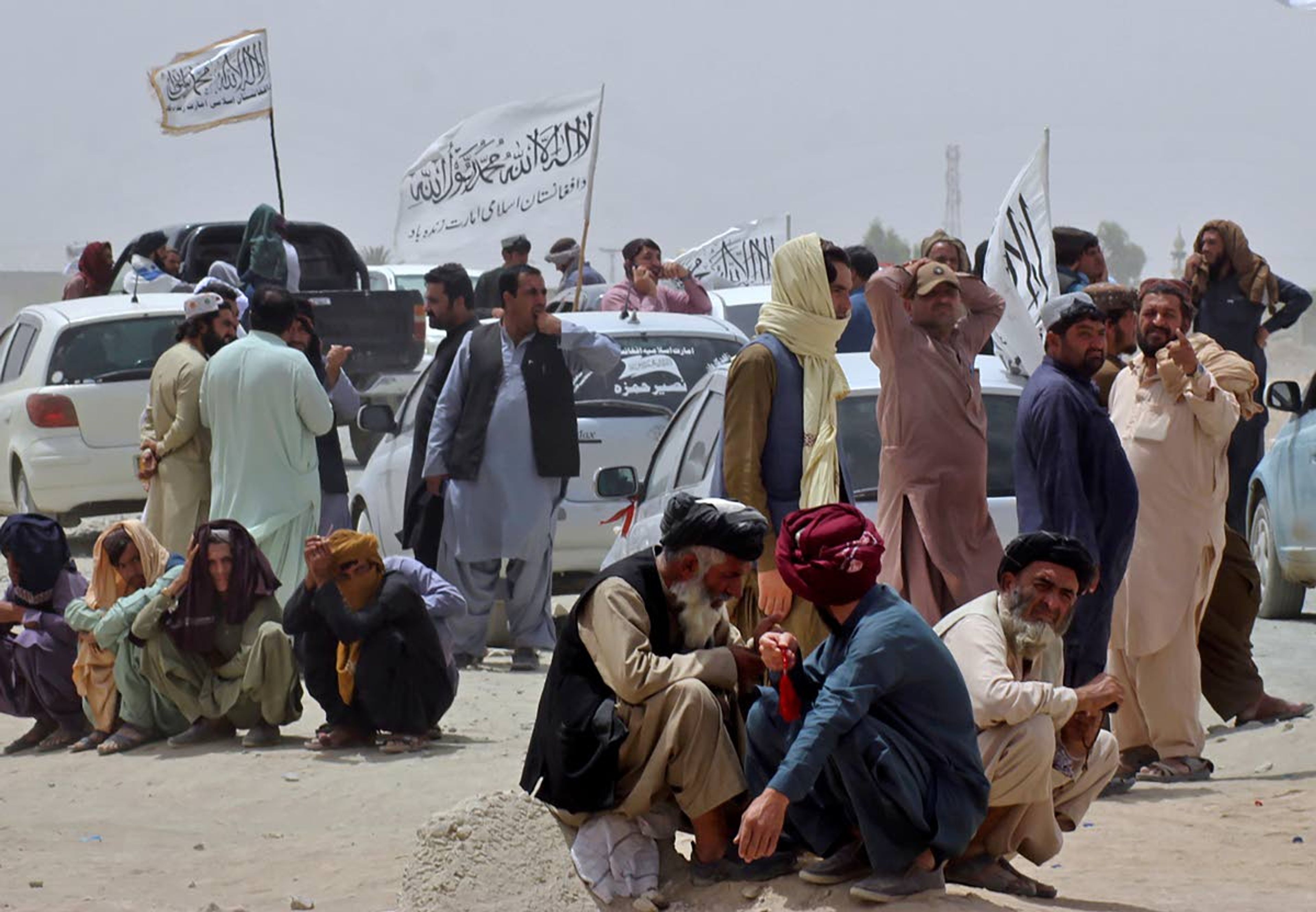 People near Taliban signature white flags wait for the arrival of their relatives, who were reportedly released from prison by the Taliban in Afghanistan, at a border crossing point, in Chaman, Pakistan, Tuesday, Aug. 17, 2021. (AP Photo/Jafar Khan)