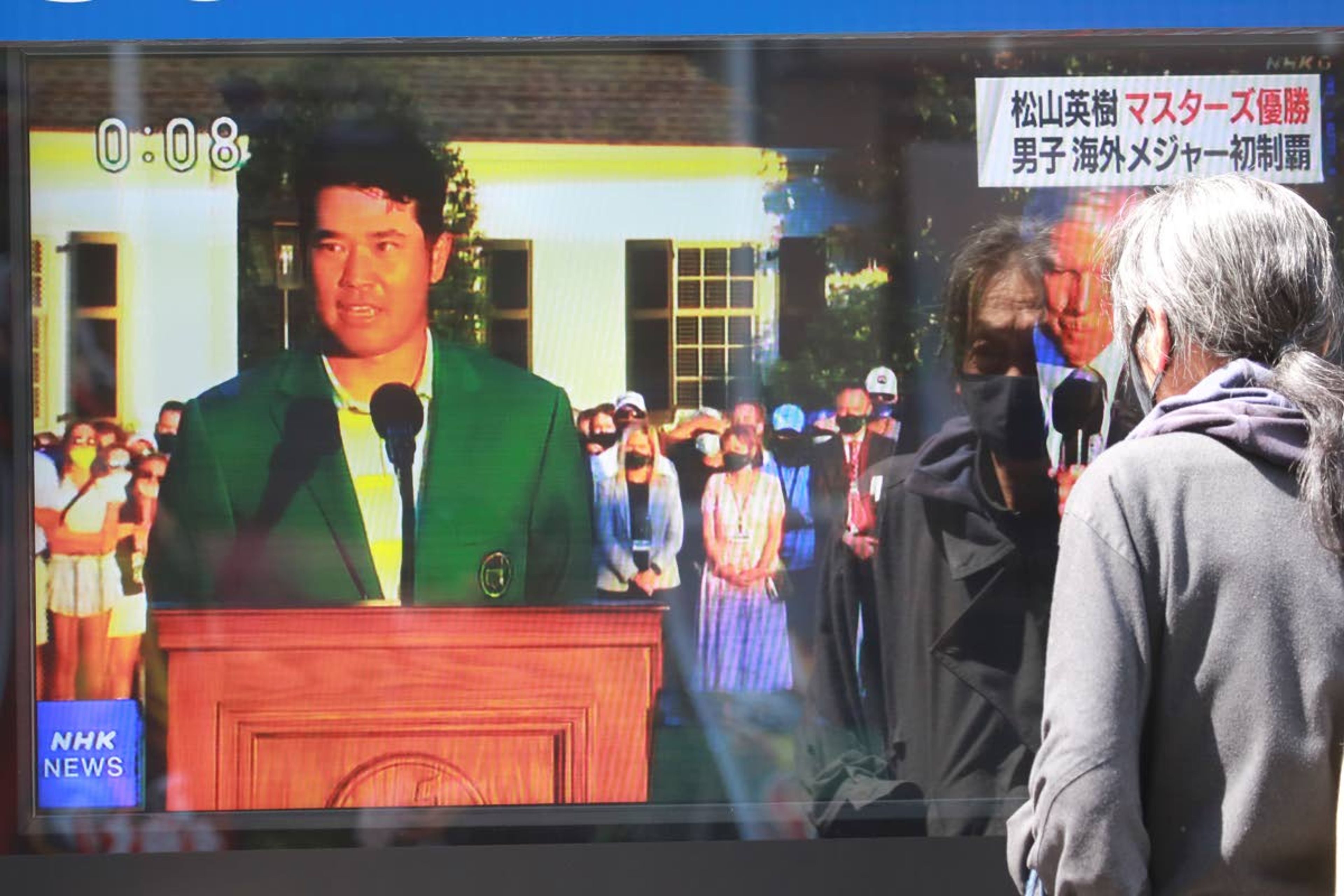 A passerby watches a tv news report showing Japanese golfer Hideki Matsuyama in the Masters, in Tokyo, Monday, April 12, 2021. From Japan's prime minister on down, the country celebrated Matsuyama's victory in the Masters — the first Japanese to win at Augusta National and wear the famous green jacket.(AP Photo/Koji Sasahara)