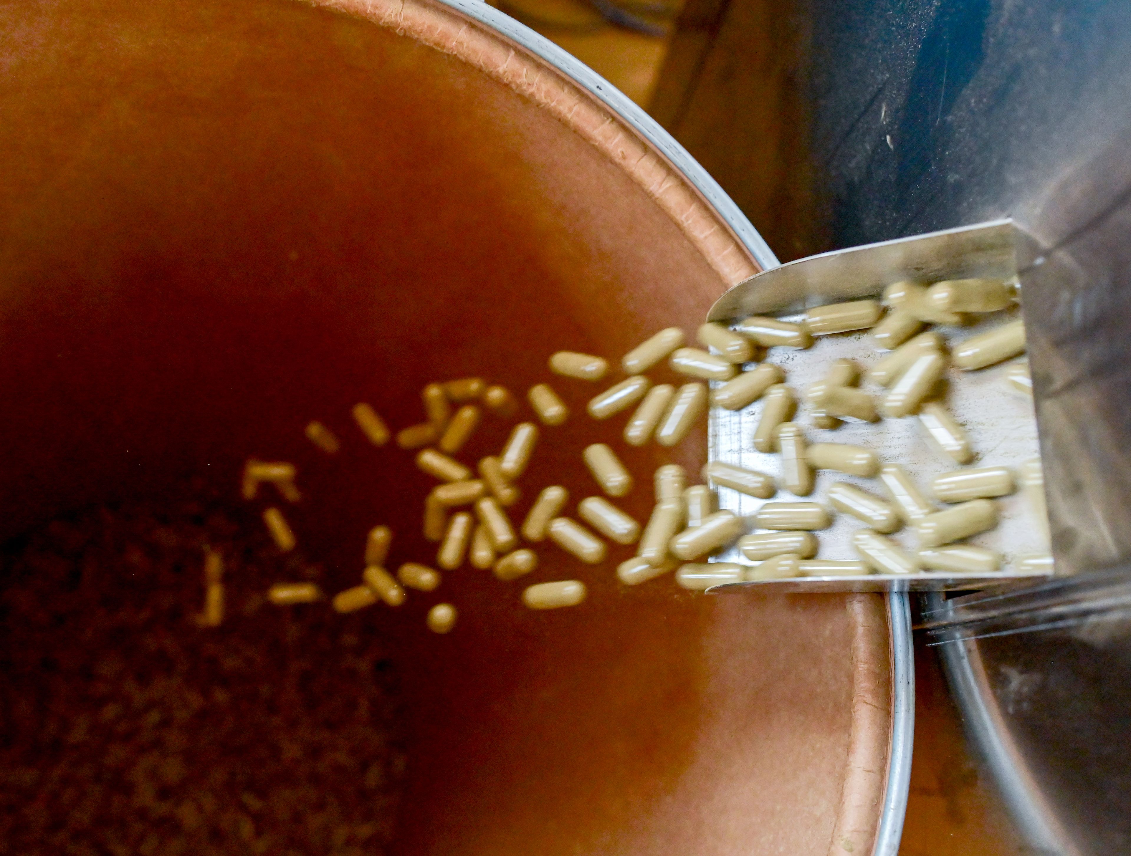 Capsules filled with kratom fall from a machine used to close the capsules Friday at Kratom Kings in Moscow.