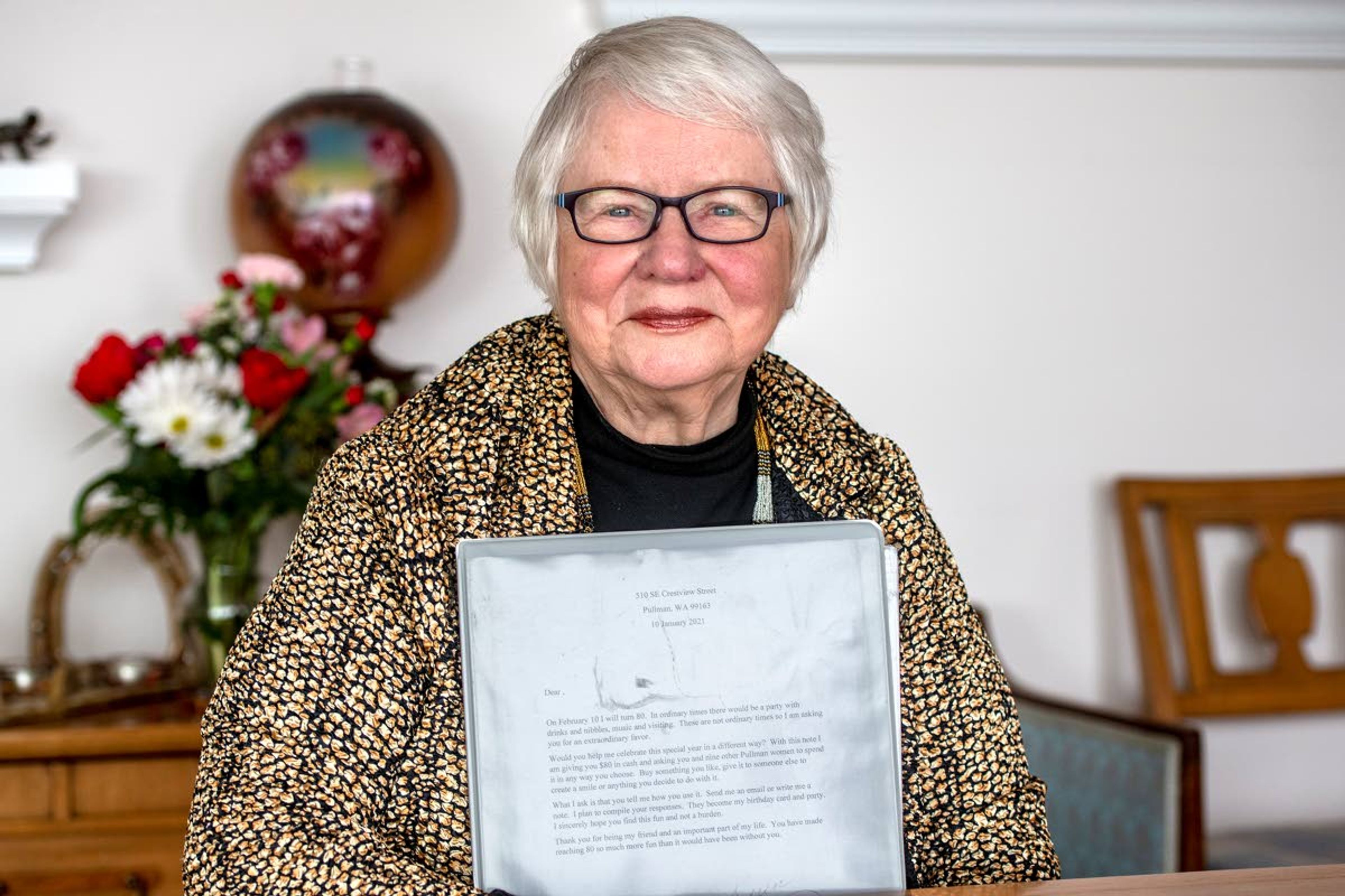 Former mayor of Pullman, Karen Kiessling, poses for a photo as she holds a scrapbook containing a letter she sent to friends as well as their responses at the dining room table at her home on Friday afternoon. Kiessling was hindered from celebrating her 80th birthday with friends and family on Feb. 10, 2021, so she adapted by sending out a letter to ten female friends that contained $80 to spend whichever way they deemed necessary, with the only request being that they must reply with how they chose to spend the money.