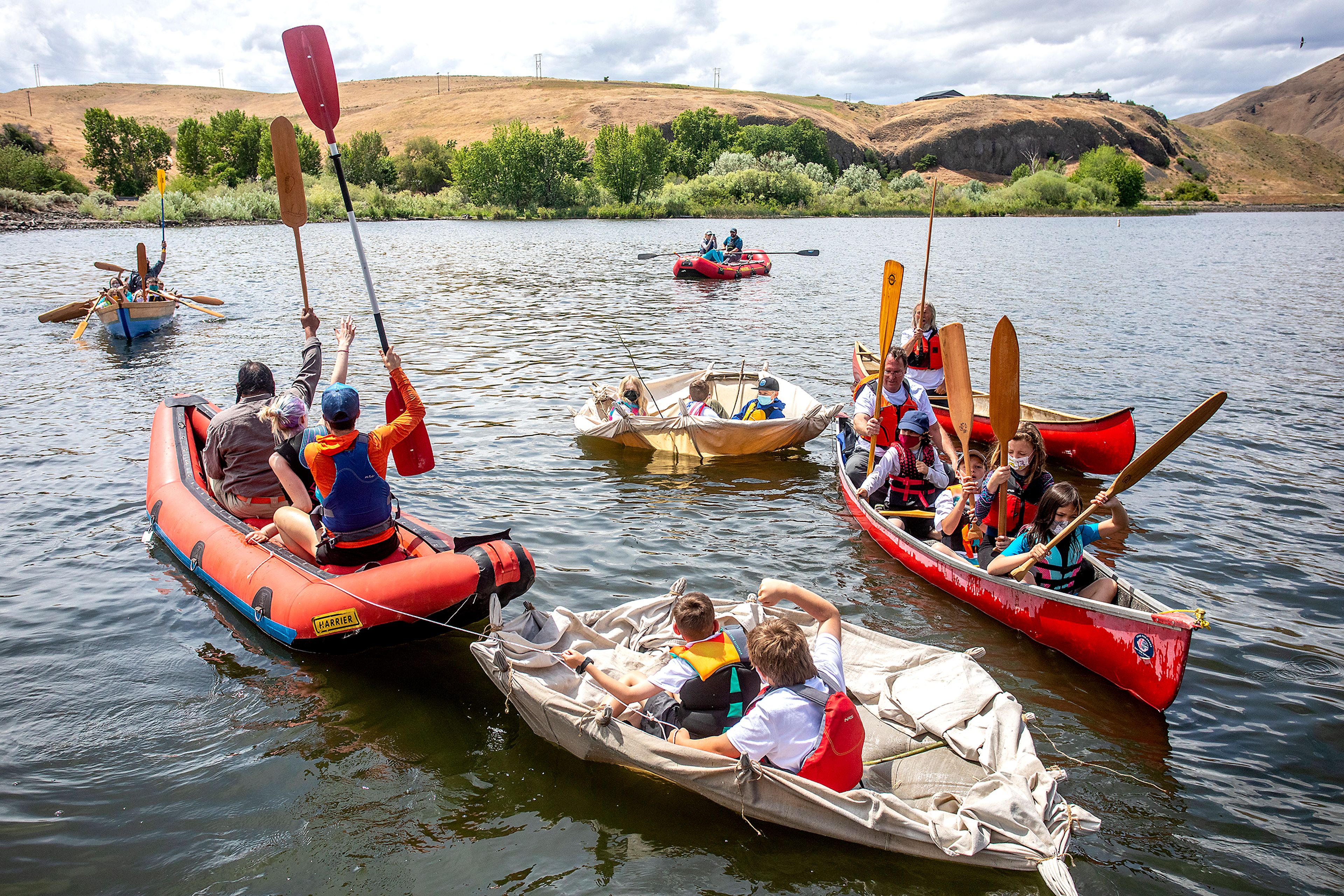 Kids from Palouse Prairie Charter School and others raise their oars in the air as they celebrate the three bull boats they made, being pulled behind other boats, successfully floating on the water on Monday. “The boat is the icing on the cake of all the knowledge these children now carry and can bring home to their family,” Garry Dorr said,