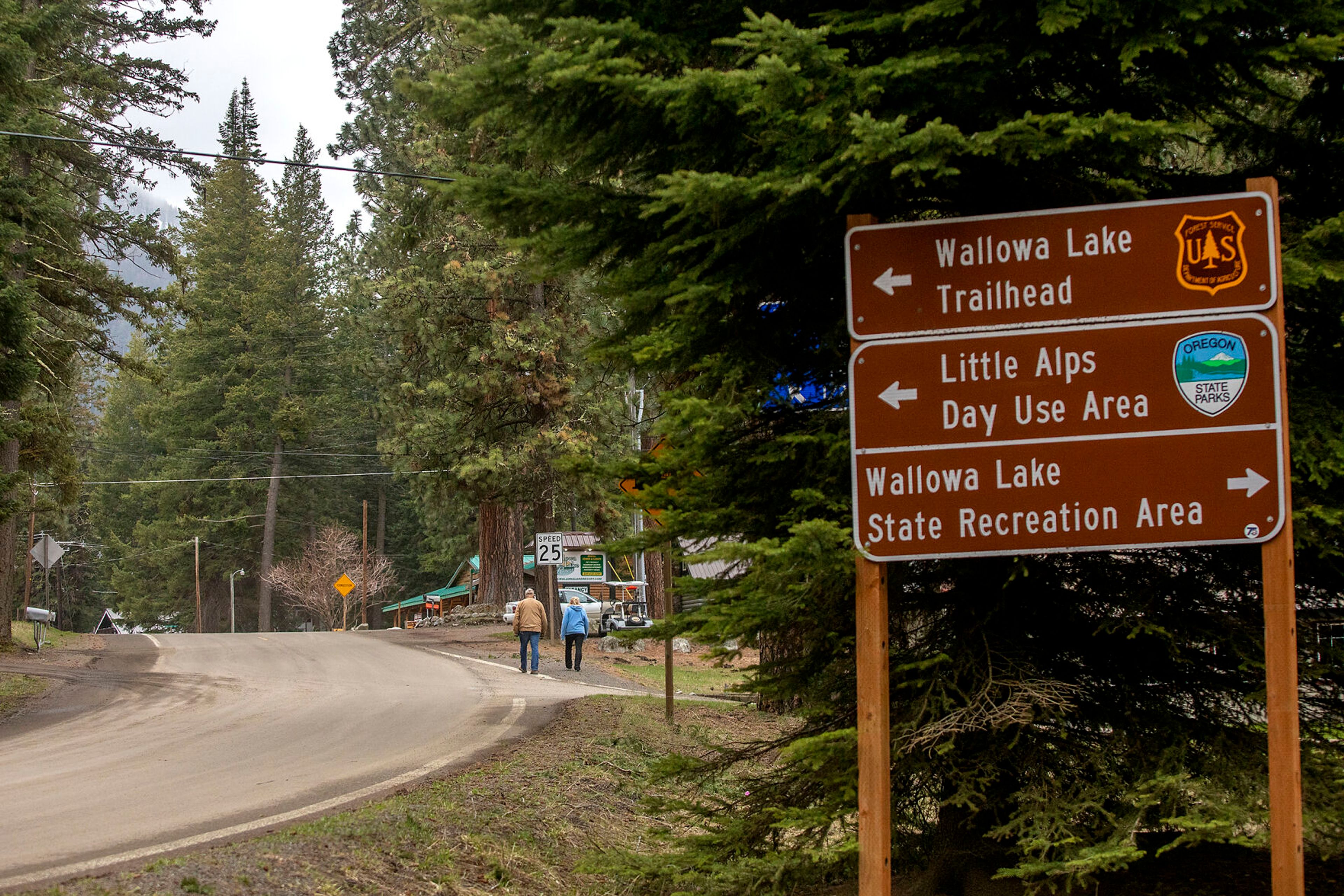 Signs direct travelers to different recreation surrounding the Wallowa Lake area as people walk along the side of the road.