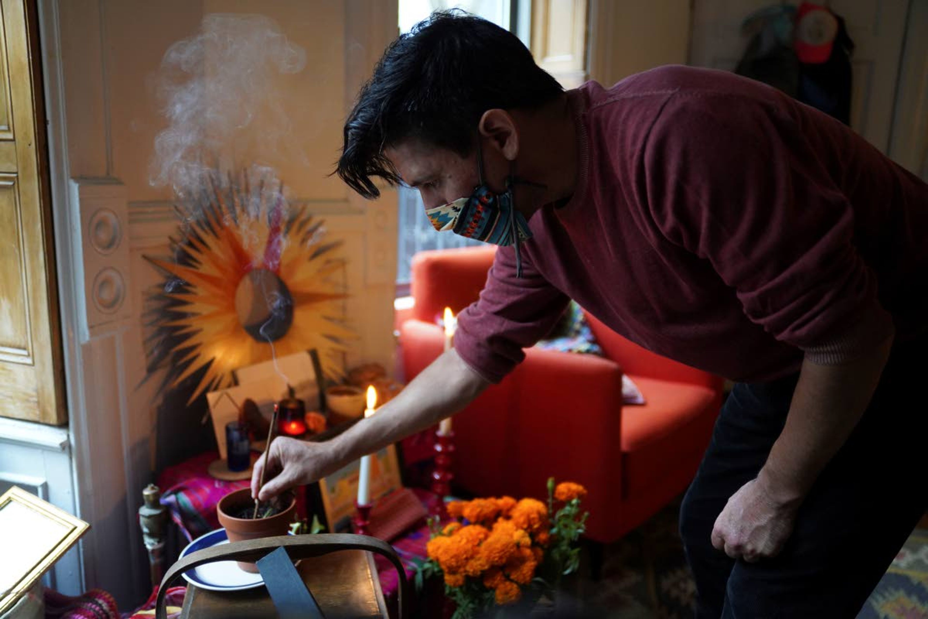 Sebastian Diaz Aguirre places incense in a Day of the Dead altar dedicated to his father, who died in a nursing home in Mexico last month, Wednesday , Oct. 28, 2020 in the Brooklyn borough of New York "It feels extremely comforting. I do feel I have a connection with my dad," said Diaz Aguirre, who set up his first ofrenda, or altar, since moving to the U.S. eight years ago. (AP Photo/Emily Leshner)