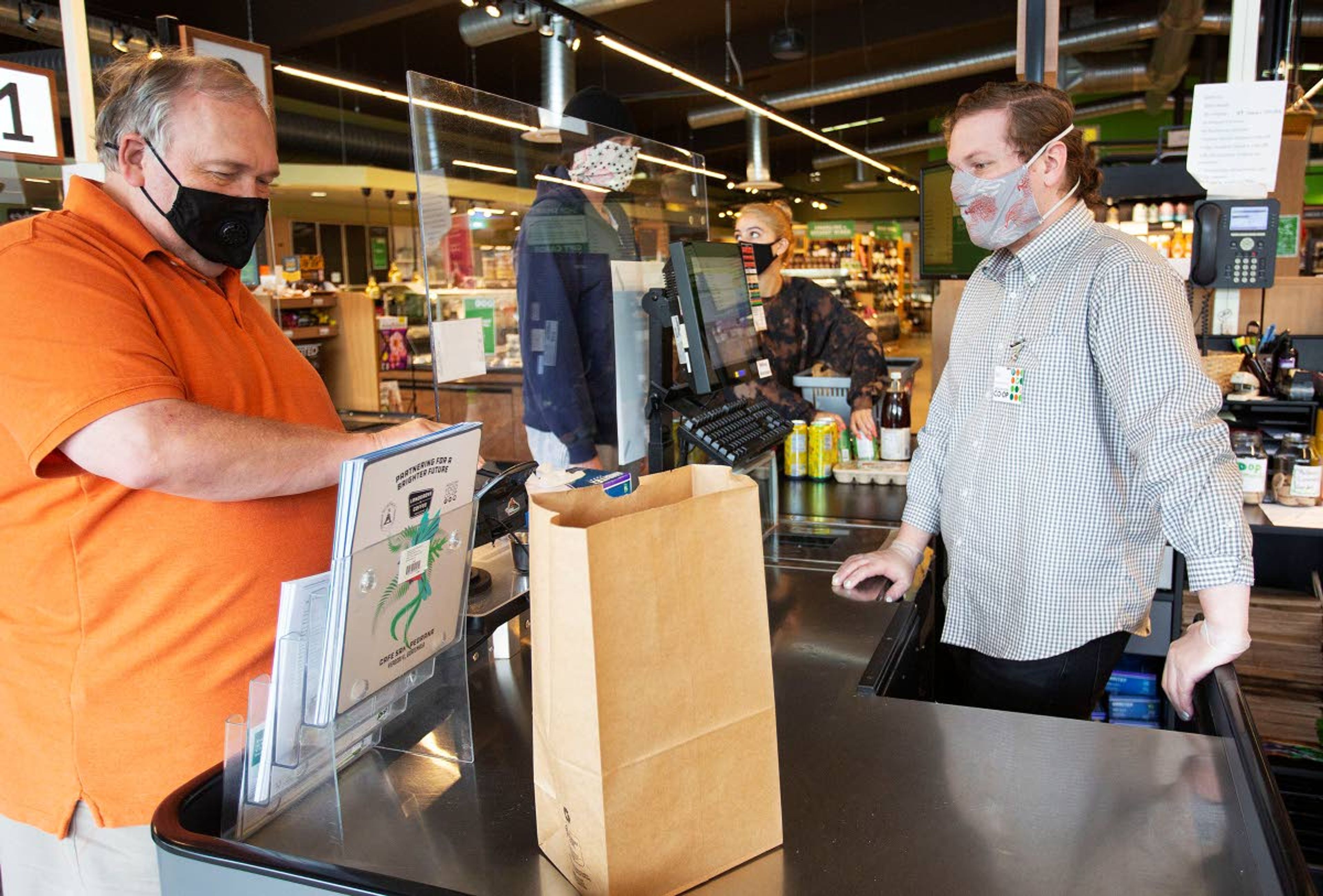 Checker Ian Pannkuk, right, wears a mask while helping a customer Wednesday at the Moscow Food Co-op.