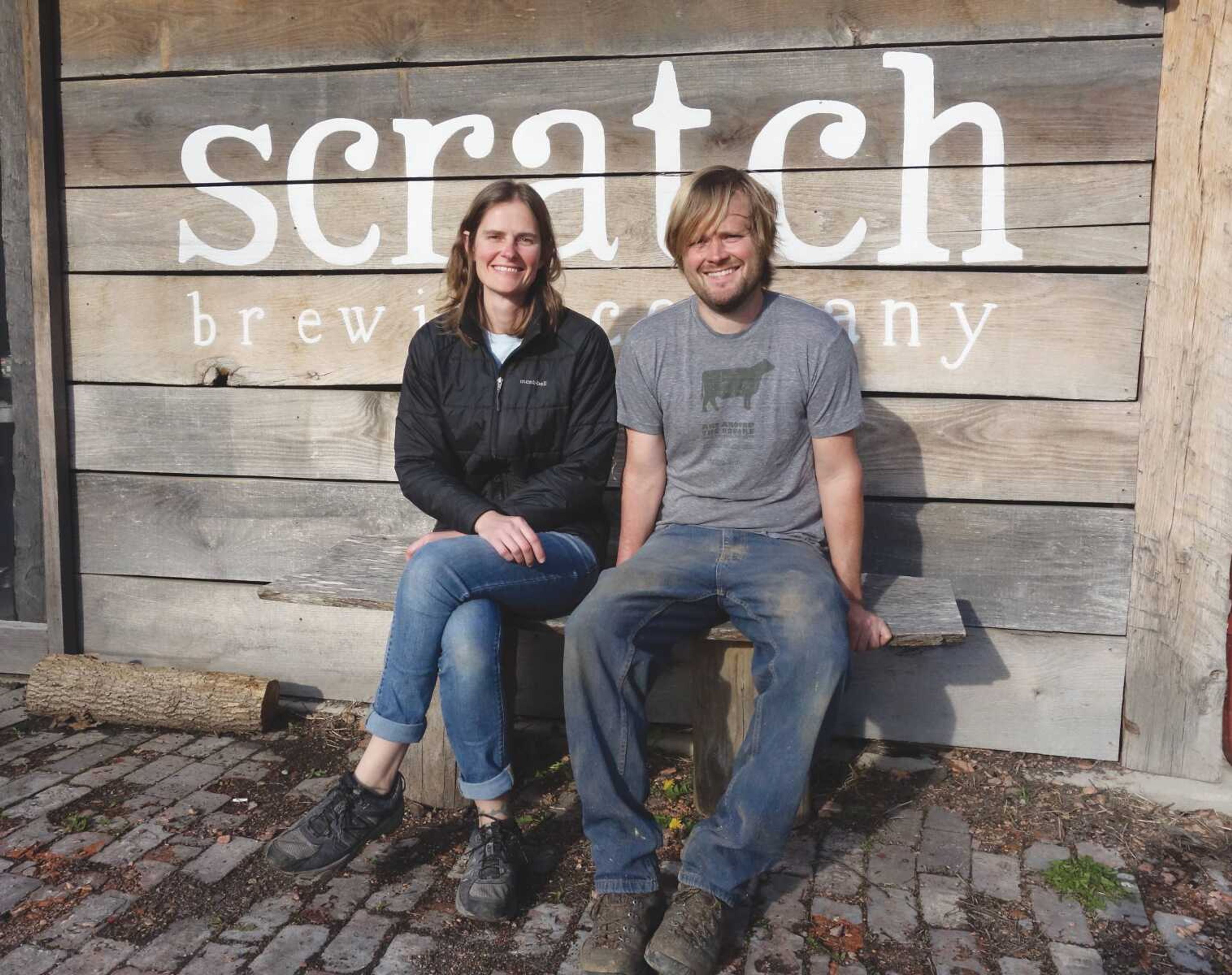 Marika Josephson and Aaron Kleidon sit in front of the Scratch Brewery sign where they try to source the ingredients for their beer from local plants.