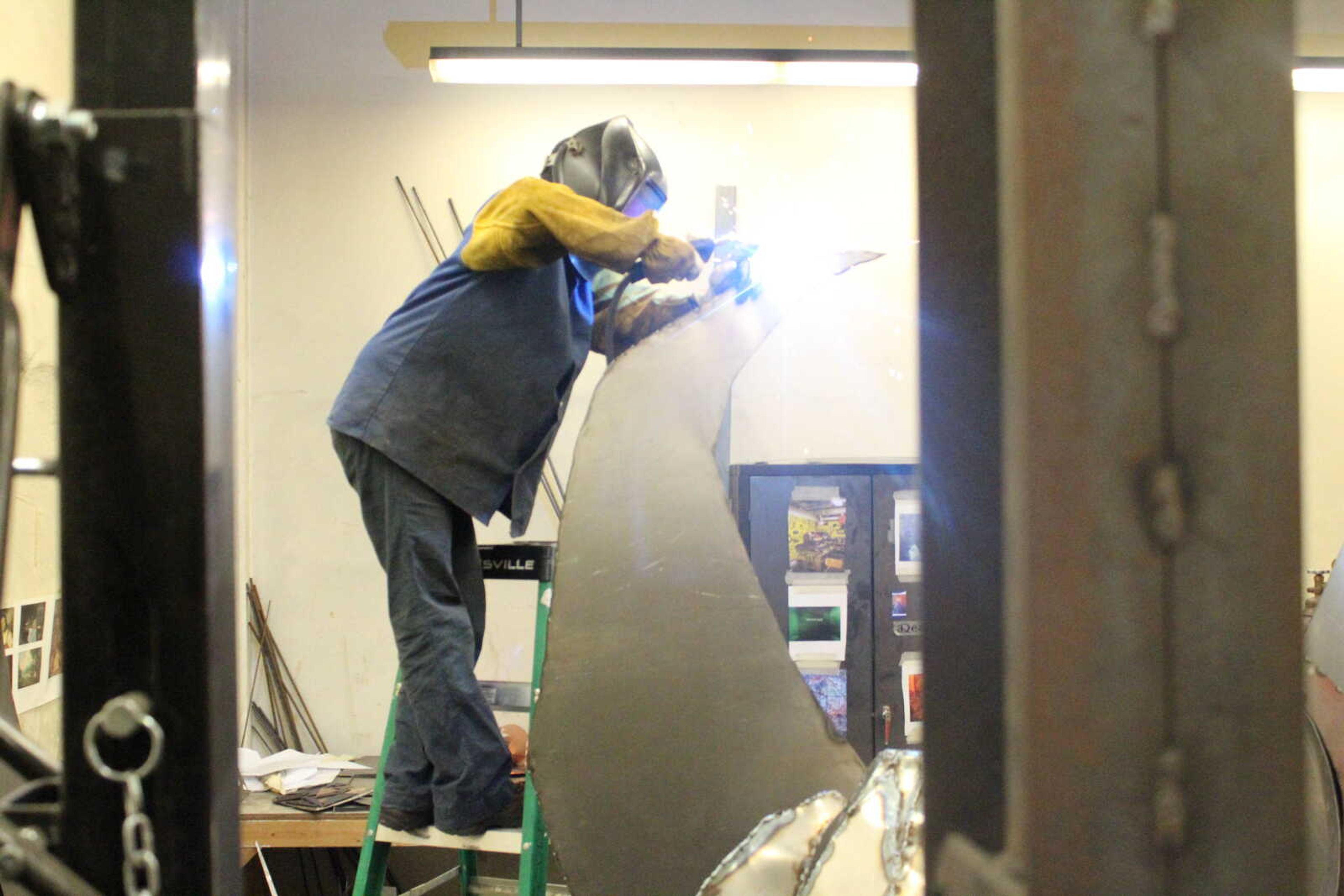 Sculpture student Deanna Hoffman stands on a ladder to weld on her newest sculpture.