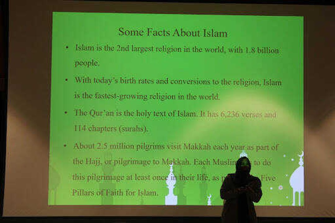 Shahd Osama stands in front of the projection screen, speaking about the information at hand. The slides changed to present different information, including the number of Muslims in the world, the pillars of Islam and more. 