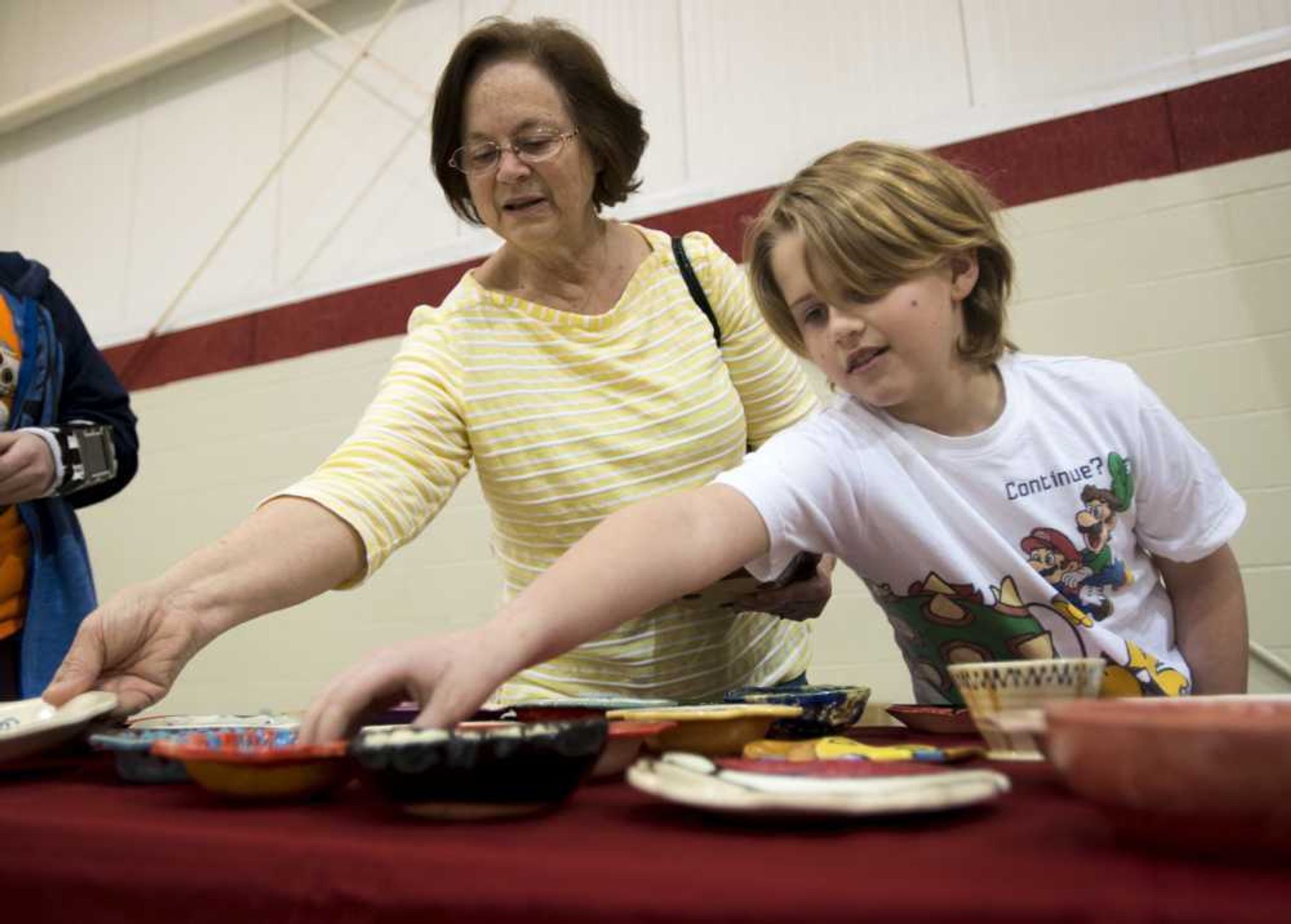 Bradyn Jaster, 8, looks at decorative bowls with his grandmother, Avon Crocker, during the Empty Bowls Banquet on Sunday.