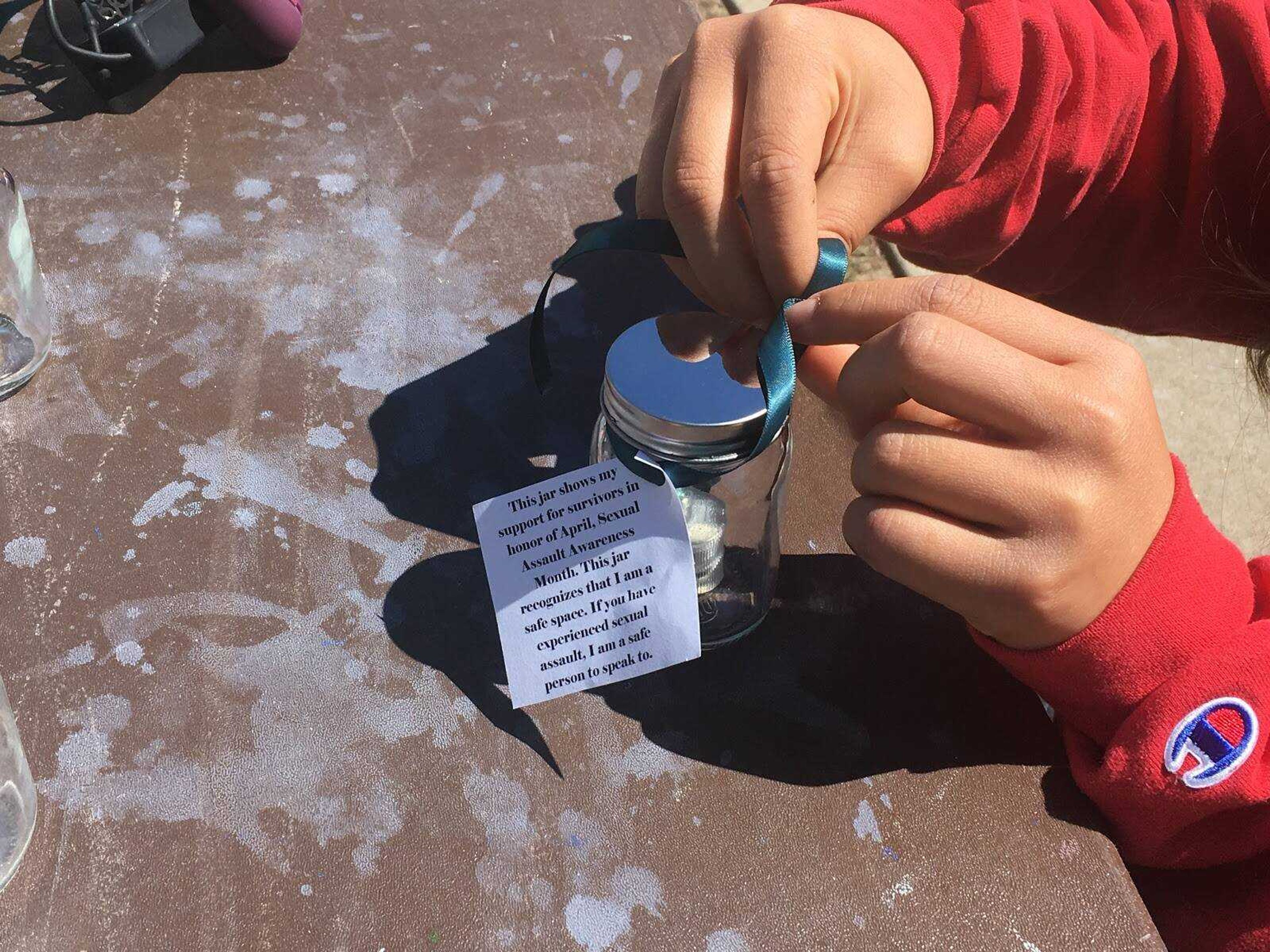 A Southeast student makes a safety jar at the booth for Sexual Assault Awareness Month. Similar to the lid, nearby trees were wrapped with teal ribbons.