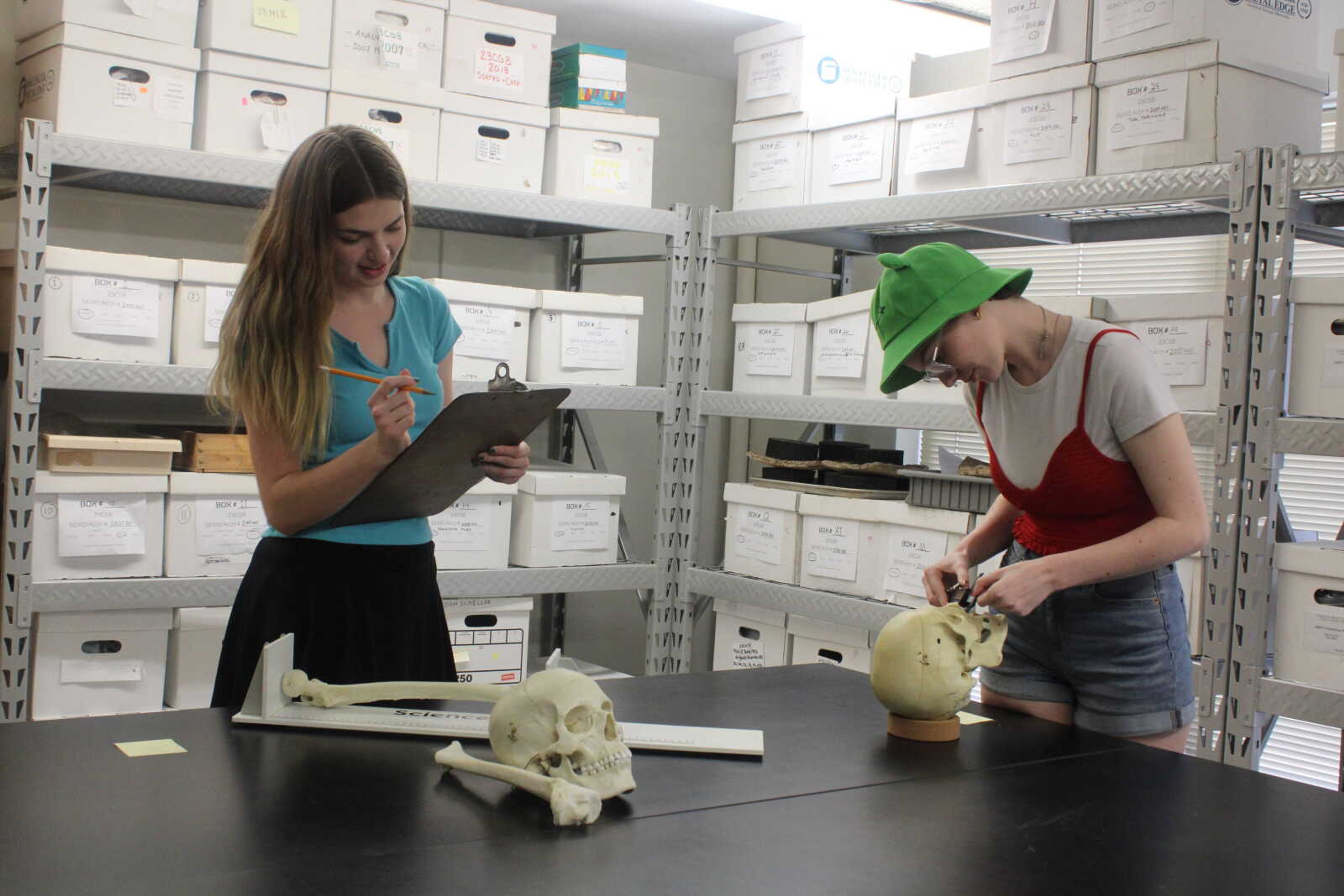 Whitney Smith (left) and Grace Sommer study and record information about different bones. Their lab room has important records and tools that help them when working on cold cases. 
