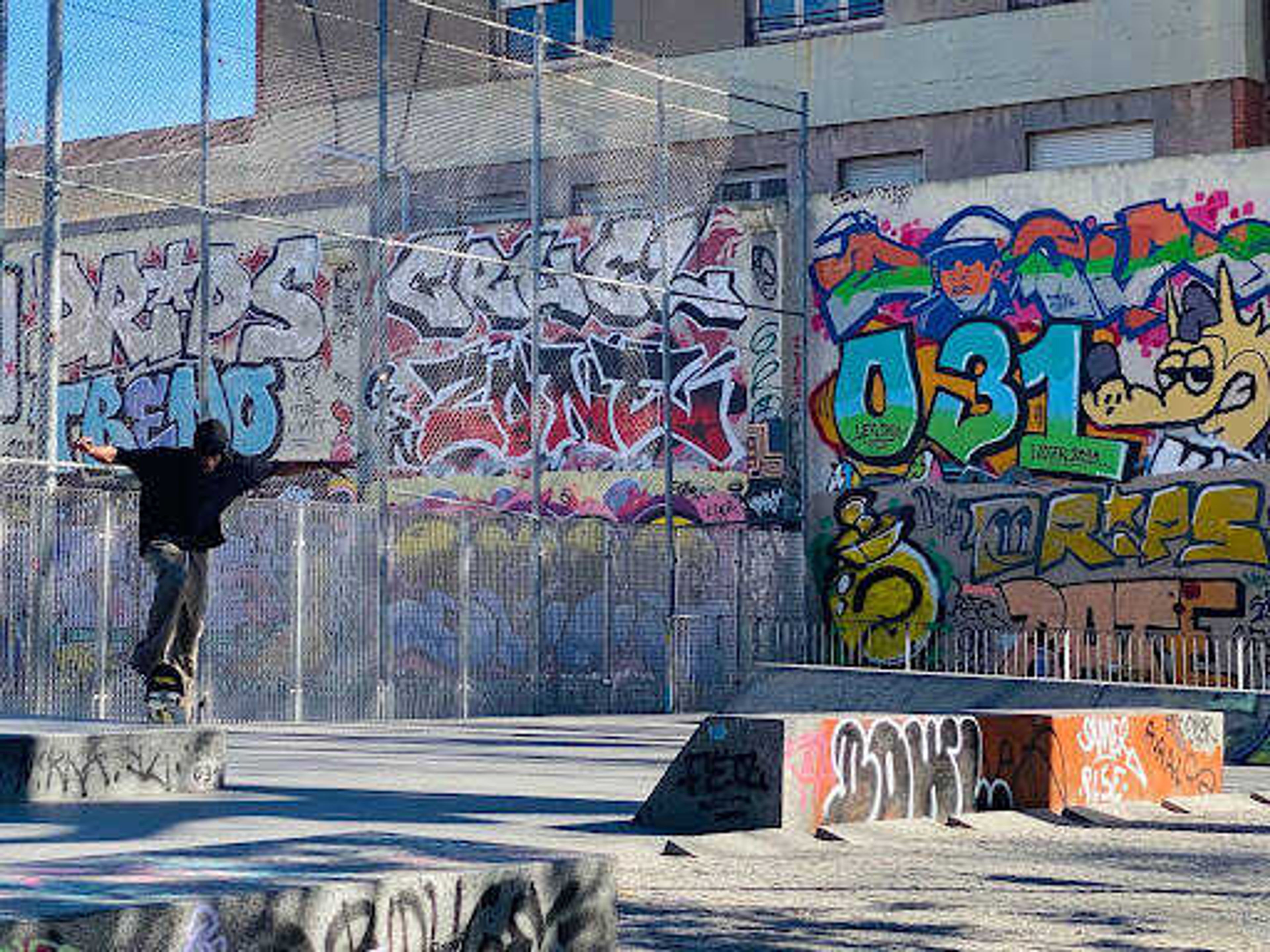A skateboarder attempts tricks in front of a graffiti wall alongside the Barcelona beach. 