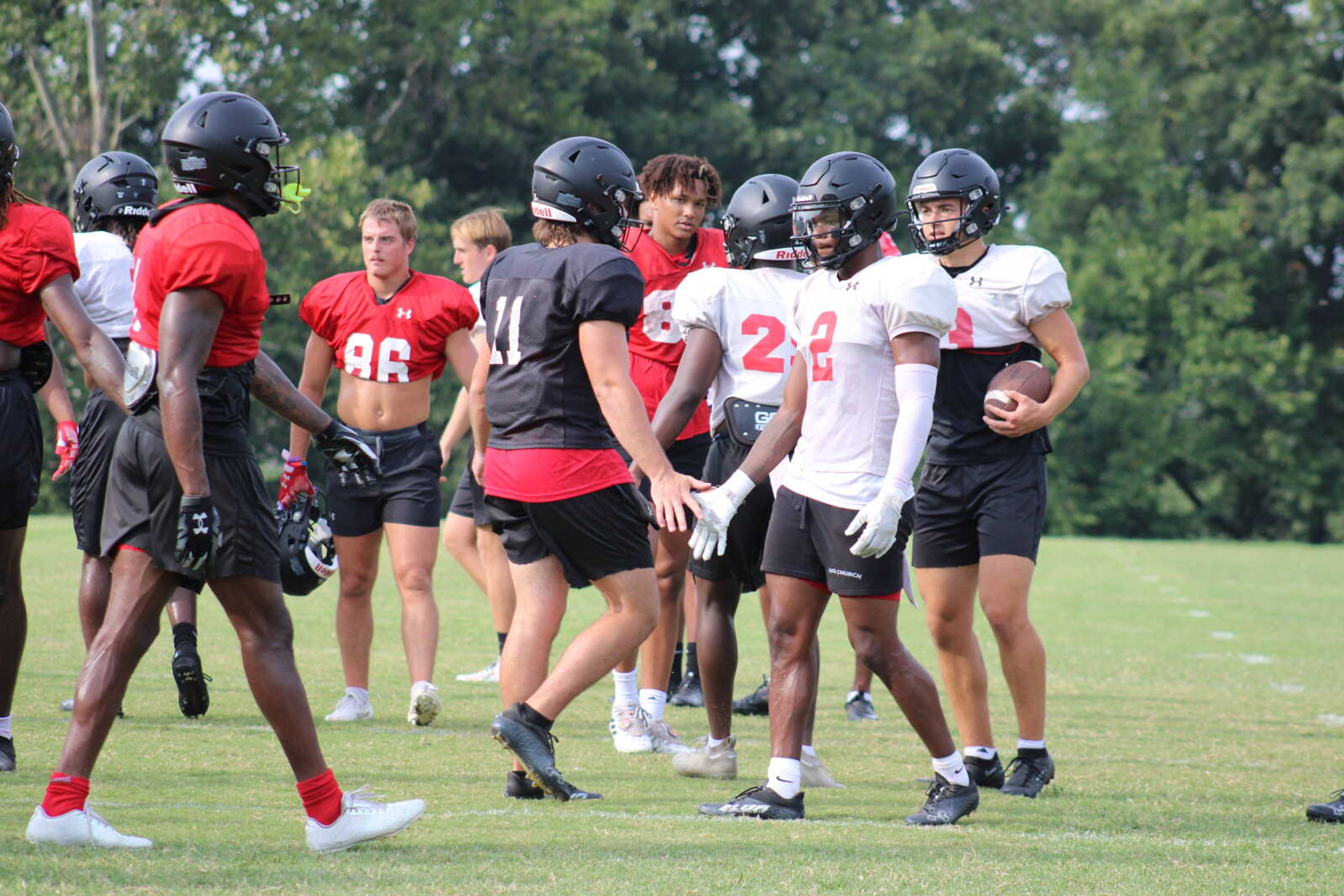 Sophomore quarterback Patrick Heitert (11, black) high-fives junior defensive back Joedrick Lewis (2, white) during a break.