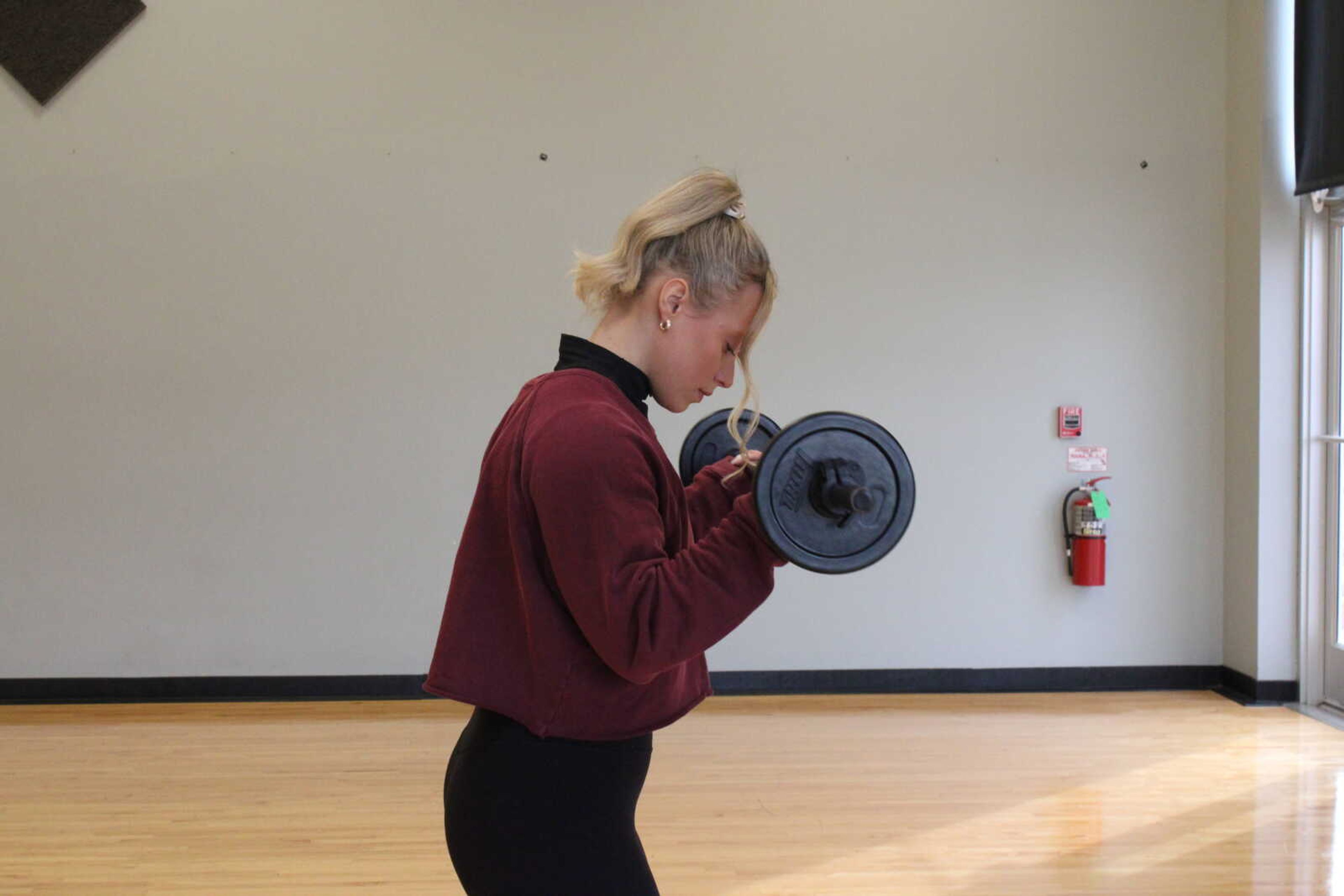 Brinkopf is performing a dumbbell curl-up. She uses this exercise to strengthen her bicep muscles in her upper arms.