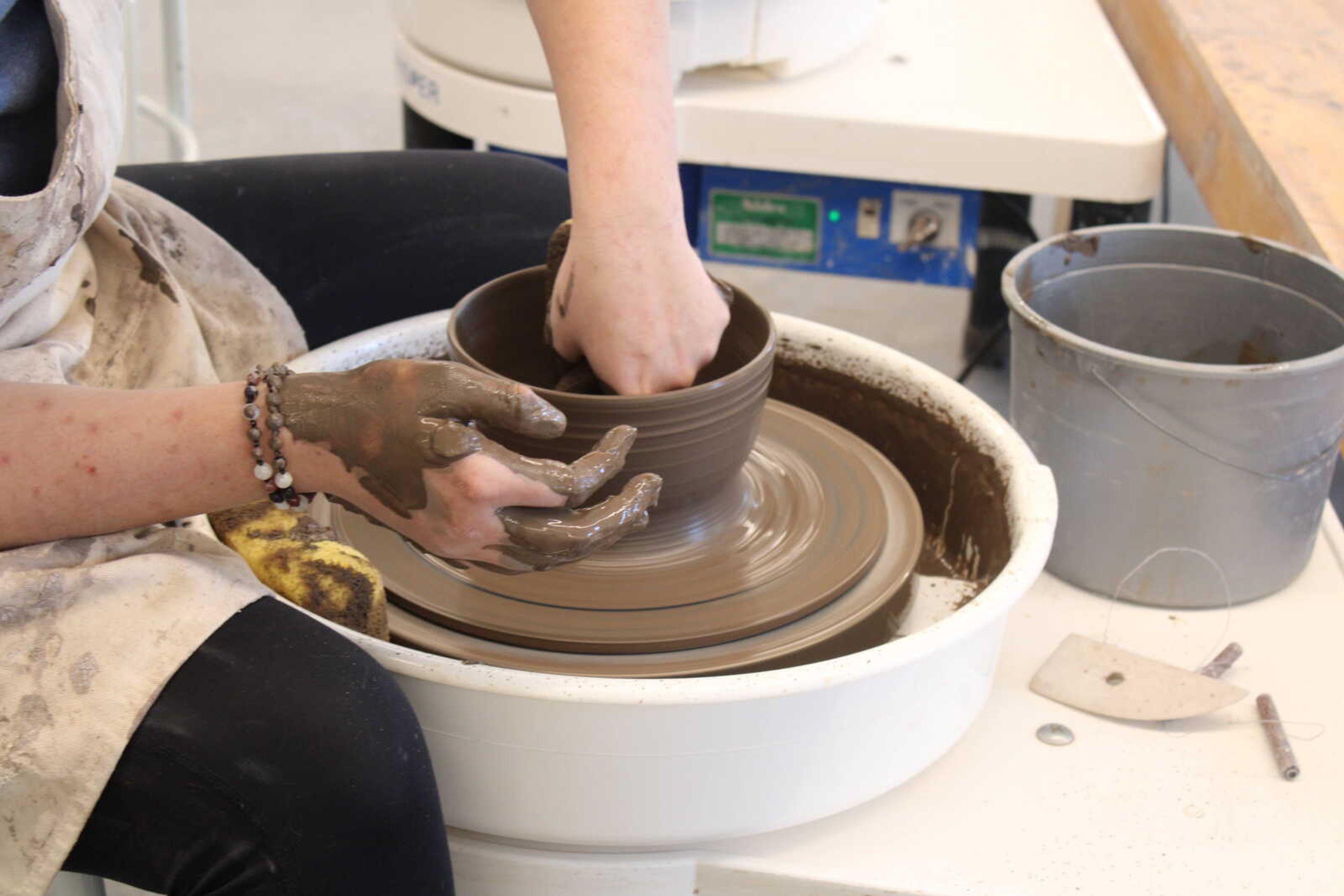 Richardson makes finishing touches to a clay bowl. She then sets the board on a shelf to dry before removing the bowl from it.
