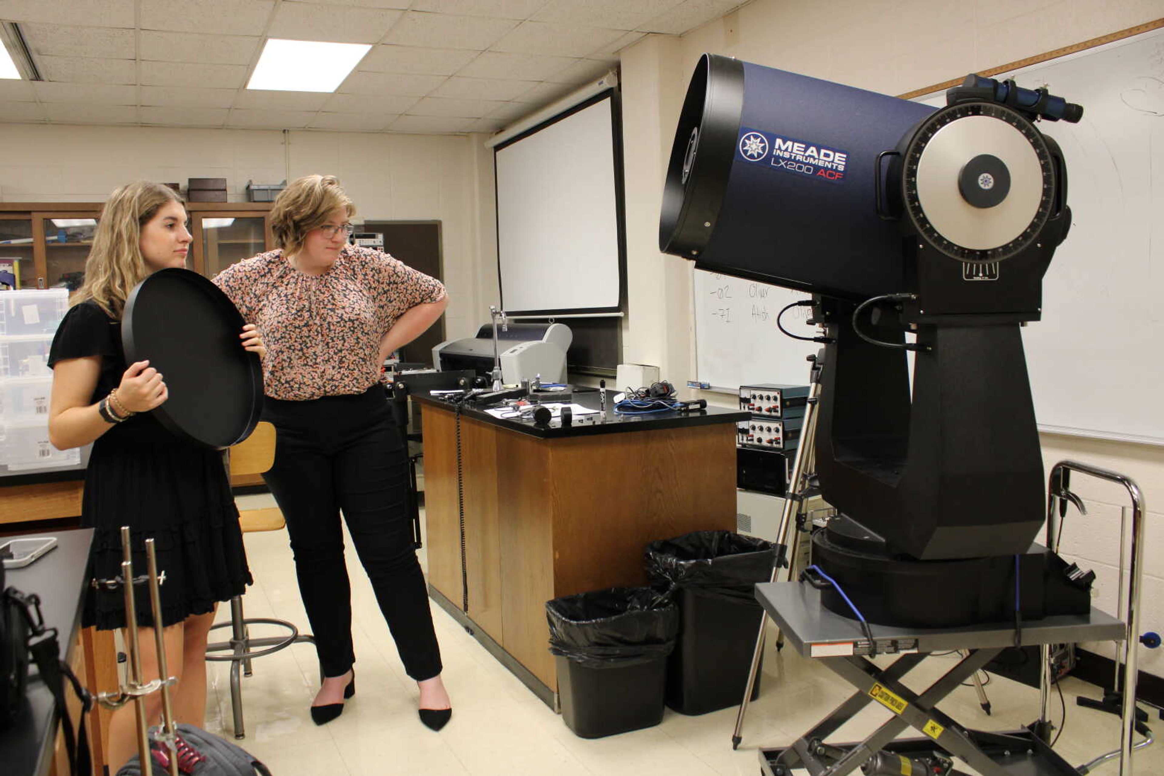 (Left) Brianna Mills and Sophia Hodge observe the new telescope in Rhodes Hall room 301 after describing more about its functions and accessibility on Sept. 21. The telescope itself weighs around 300 pounds, and the tripod that it is mounted on during setup weighs around 75 pounds.