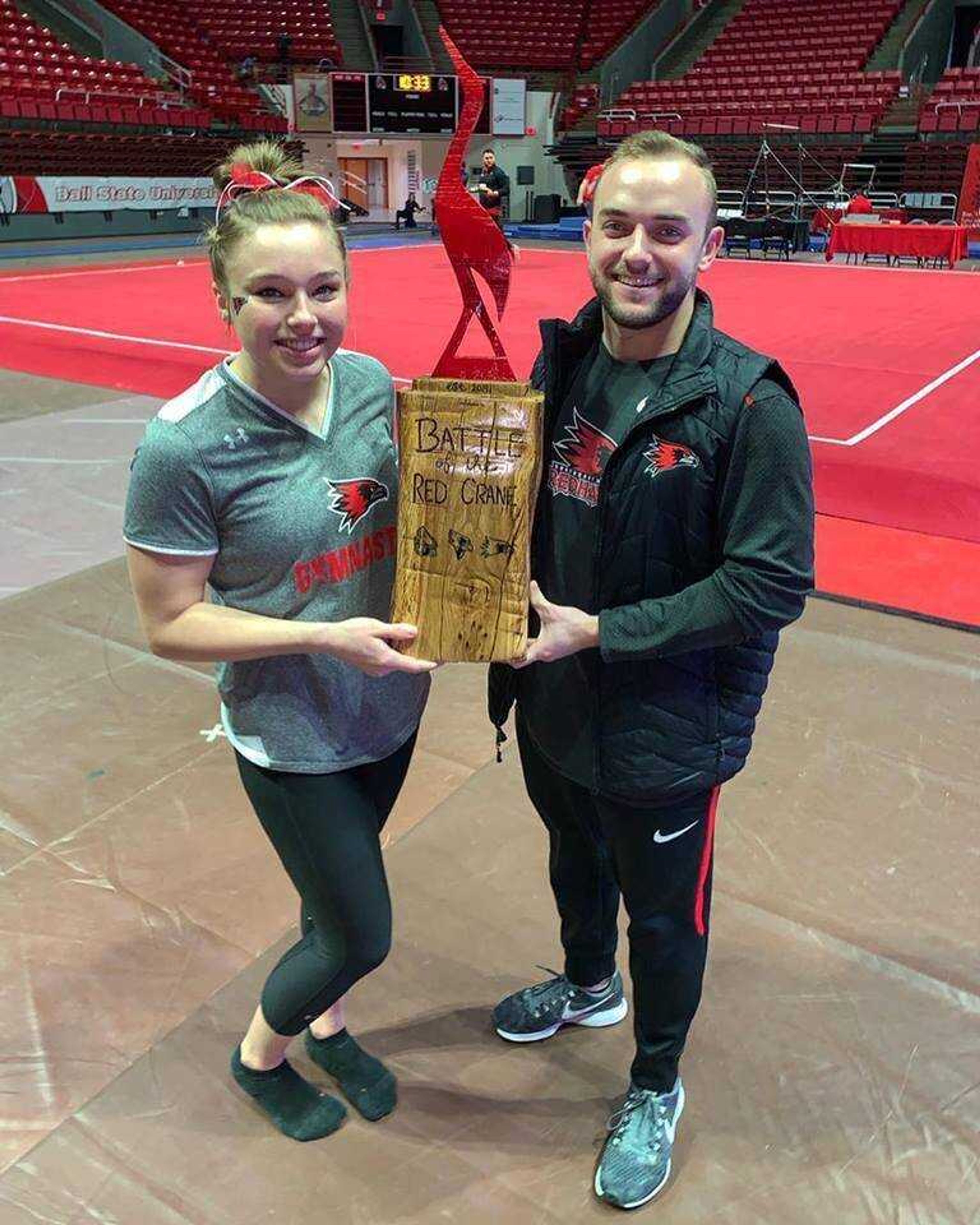 Junior gymnast Kendra Benak and assistant coach Chris Licamelli hold the trophy the two constructed for the Battle of the Red Crane.