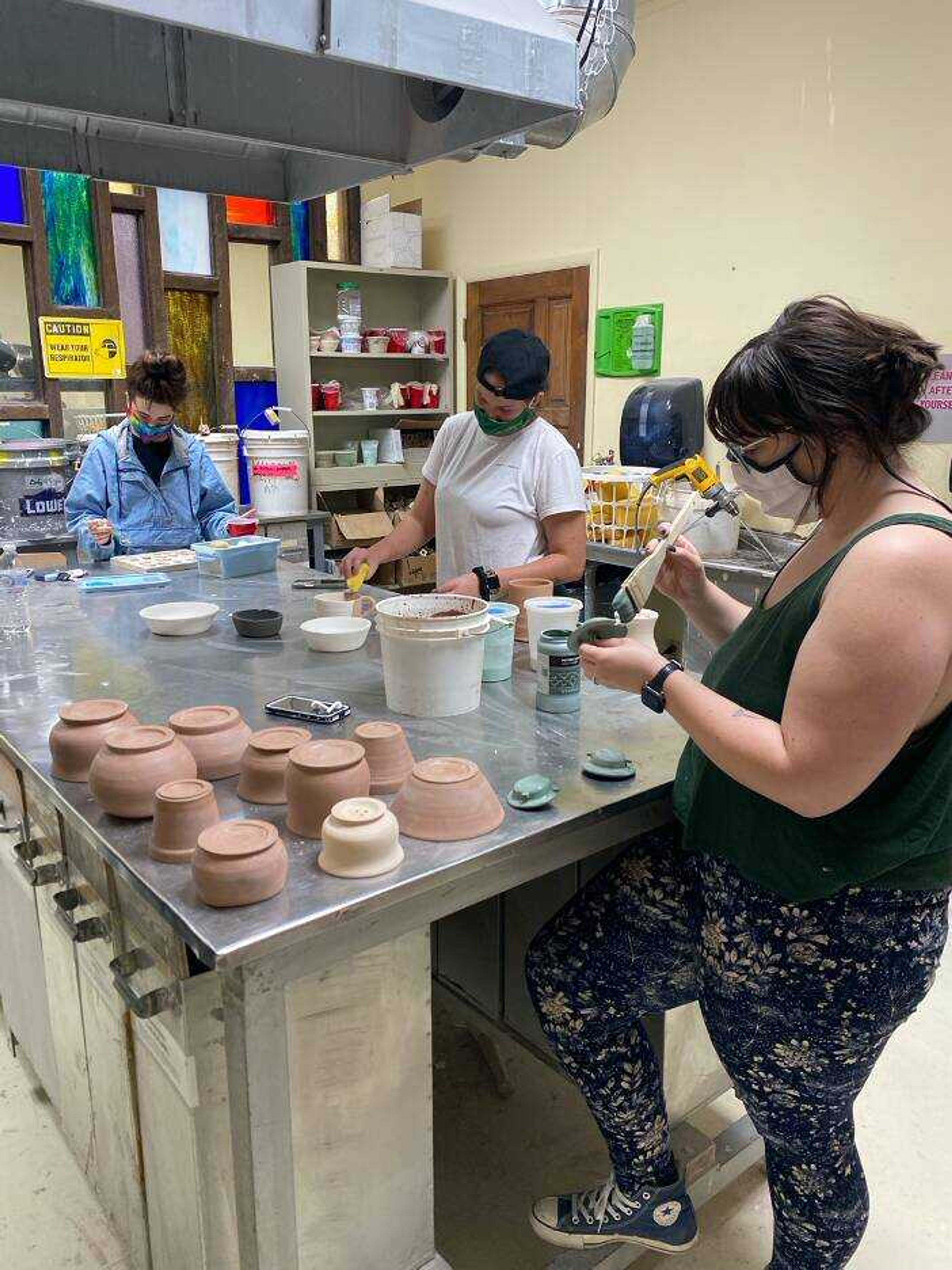 Professor Benjie Heu’s students paint glaze on lids for travel mugs in his ceramics one through five class. 