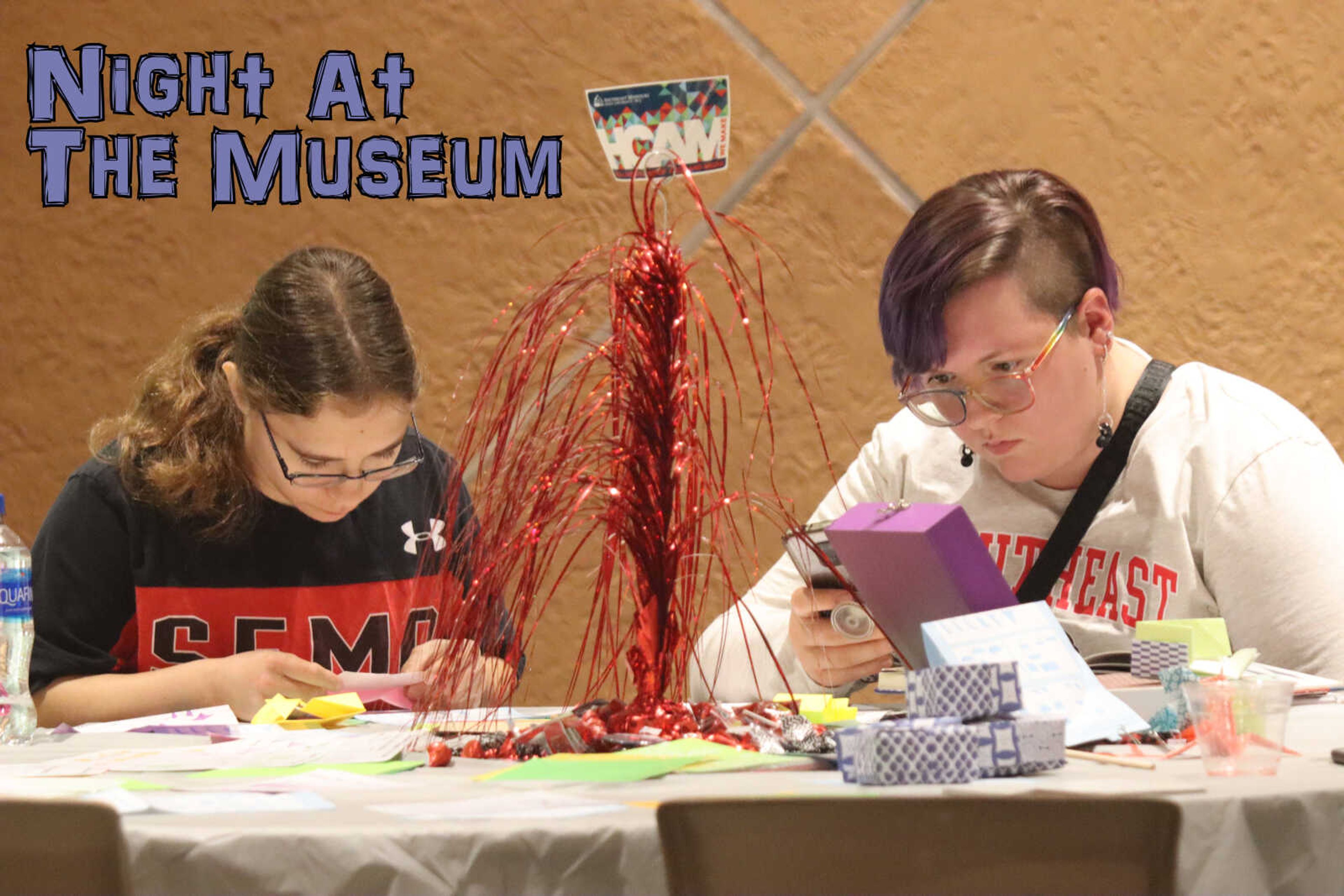 Two individuals sit at a table and participate in craft making during the Night at the Museum event hosted by Crisp Museum. 