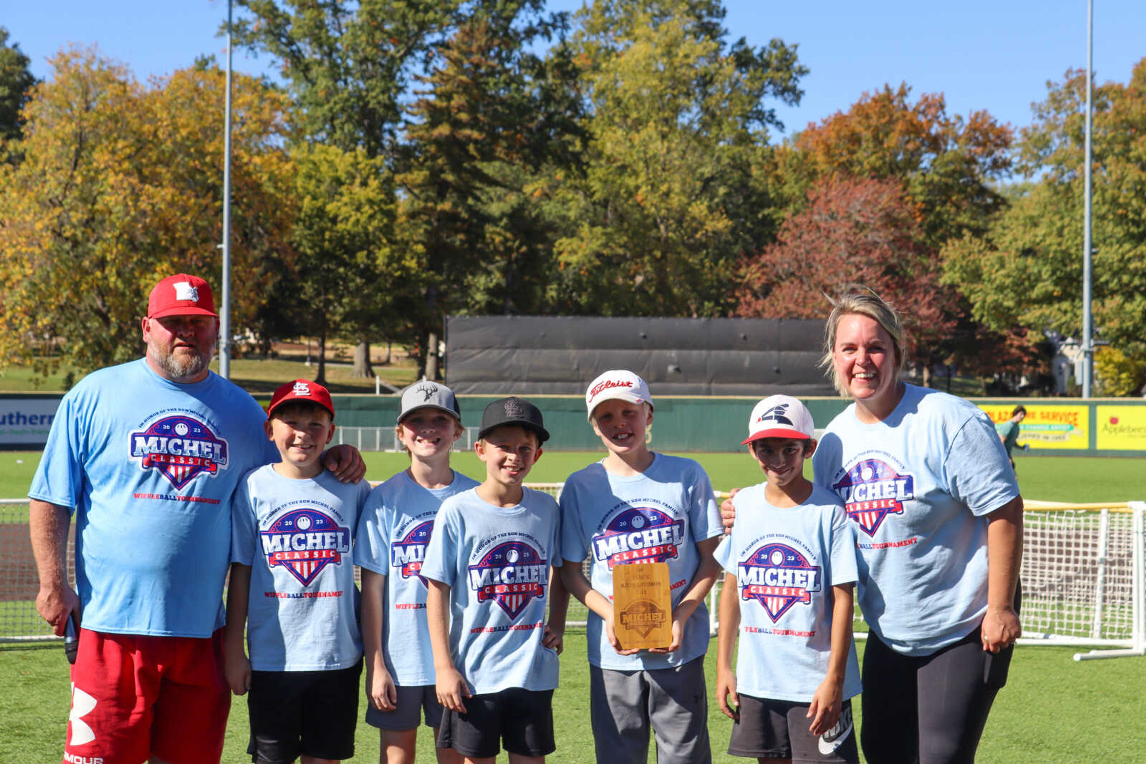 Members of the 1st place team in the 7-11 age division pose with the founders of the Michel Classic and their 1st place plaque after their victory in the championship game. The Michel Classic is a wiffleball tournament with 3 age divisions playing during different portions of the day across multiple miniature fields set up on Capaha Field.