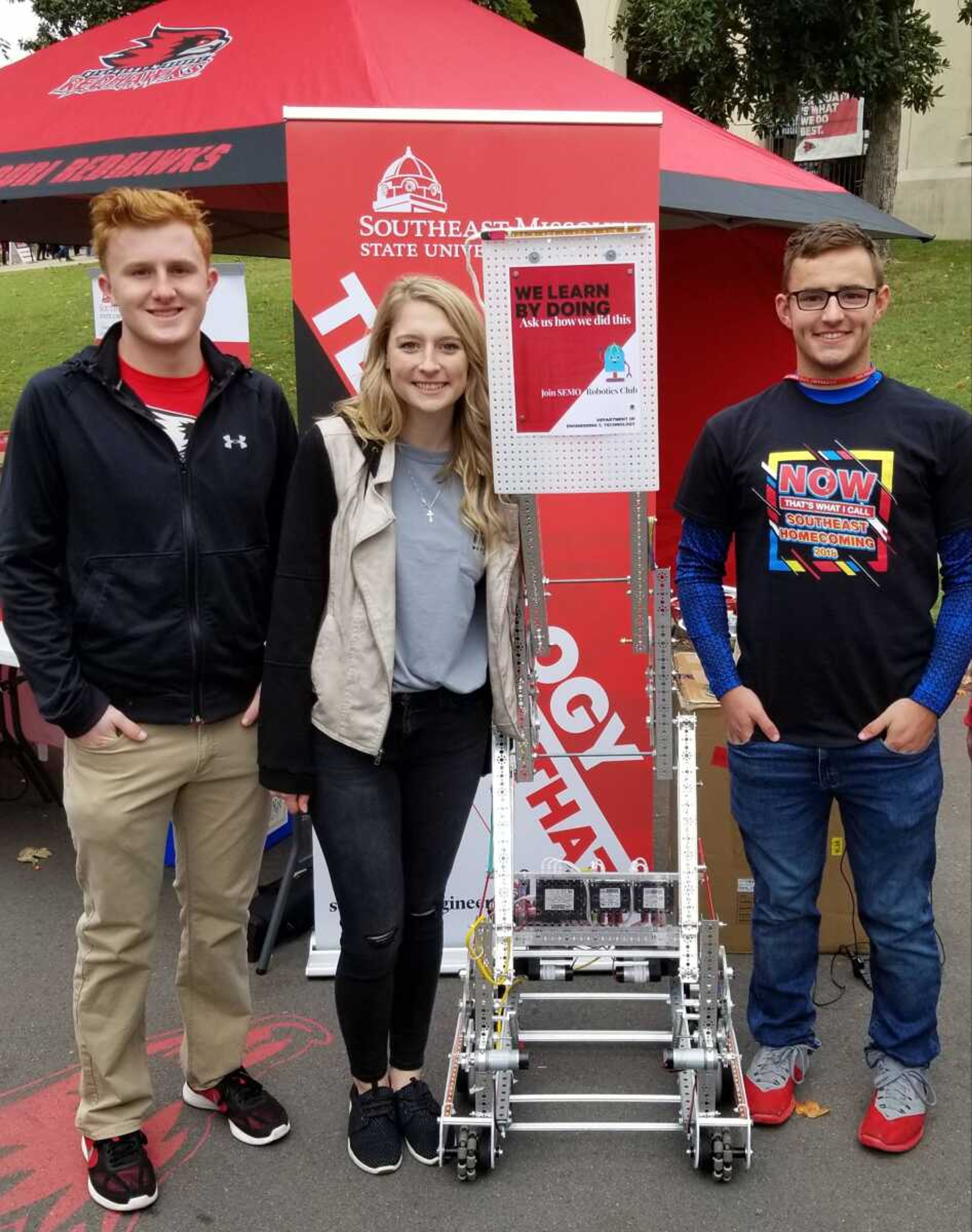Robotics club officers Nathan McKlin (UAS major); Hannah Seyer (Technology Management major); Brigham Haase (UAS major) standing with their robot during homecoming.