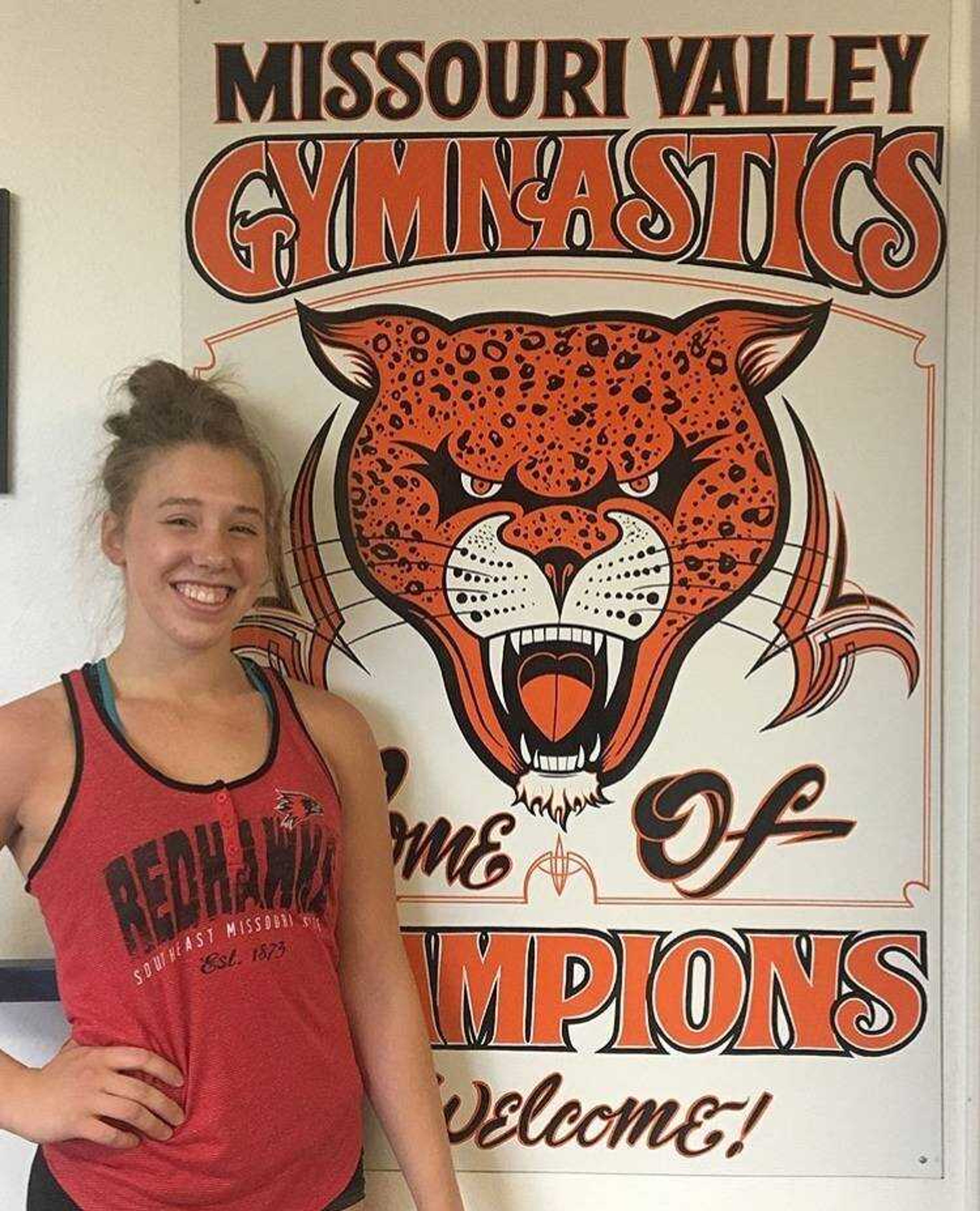 Freshman Makenzie Marciniak standing in front of a poster of her high school gymnastics program.